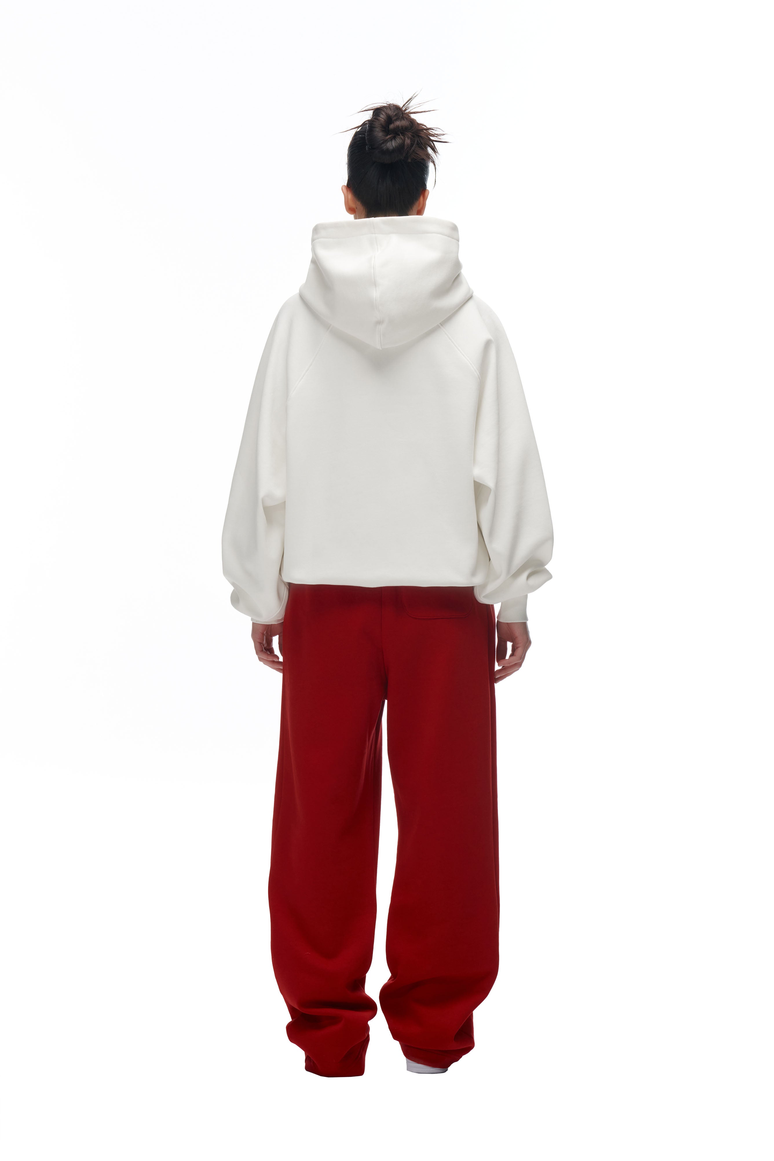 A person faces away, wearing the 6PM LH HOODIE OFFWHITE with the hood up and baggy red pants against a plain white background.