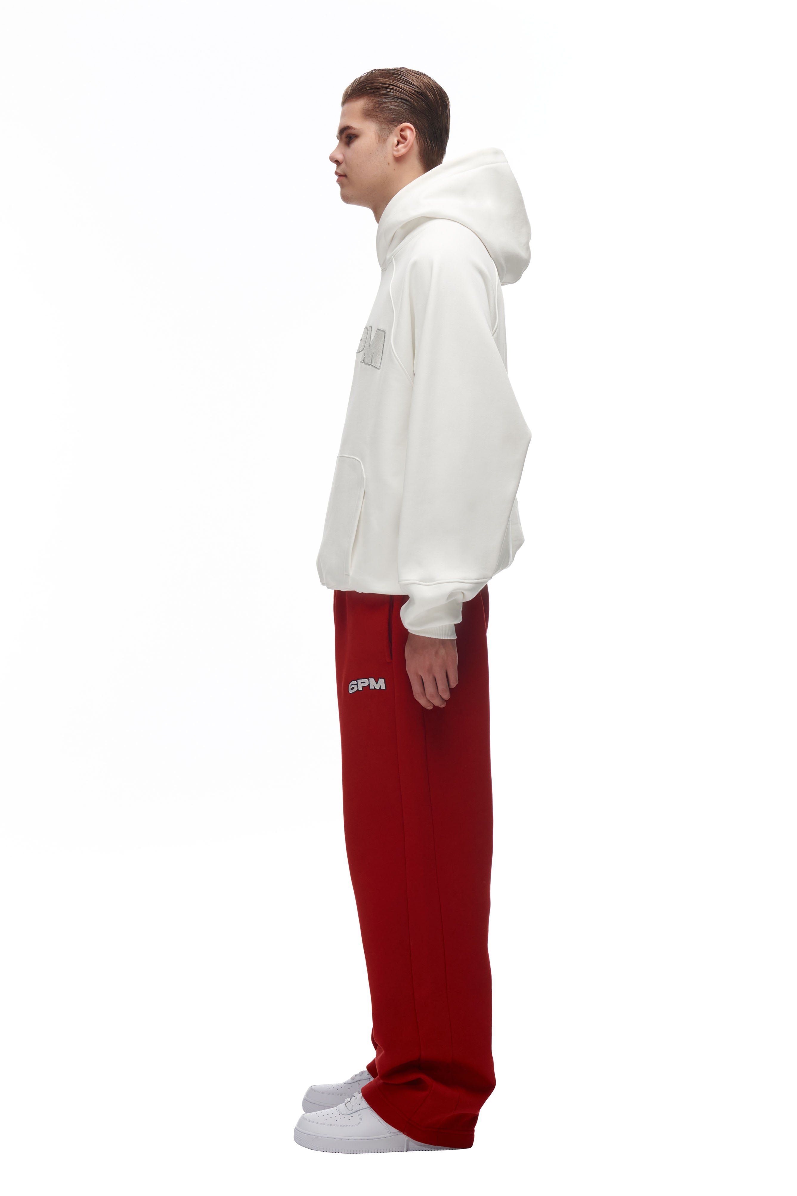 A person in profile against a white background wears the 6PM LH HOODIE OFFWHITE, red sweatpants with GPM text on the leg, and white sneakers.