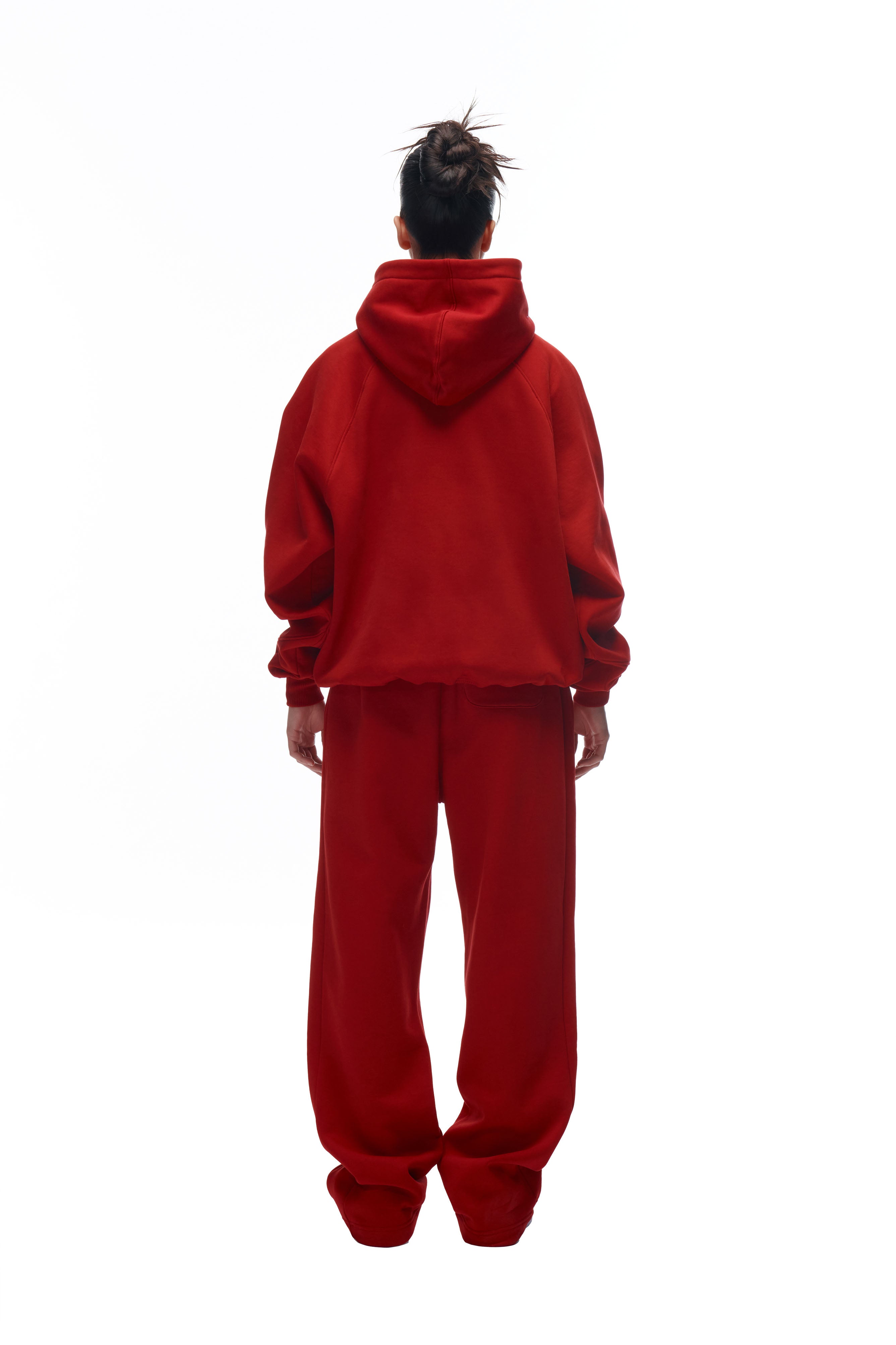 A person with their hair in a messy bun stands with their back to the camera, wearing the 6PM LH HOODIE RED and matching red sweatpants against a plain white background.