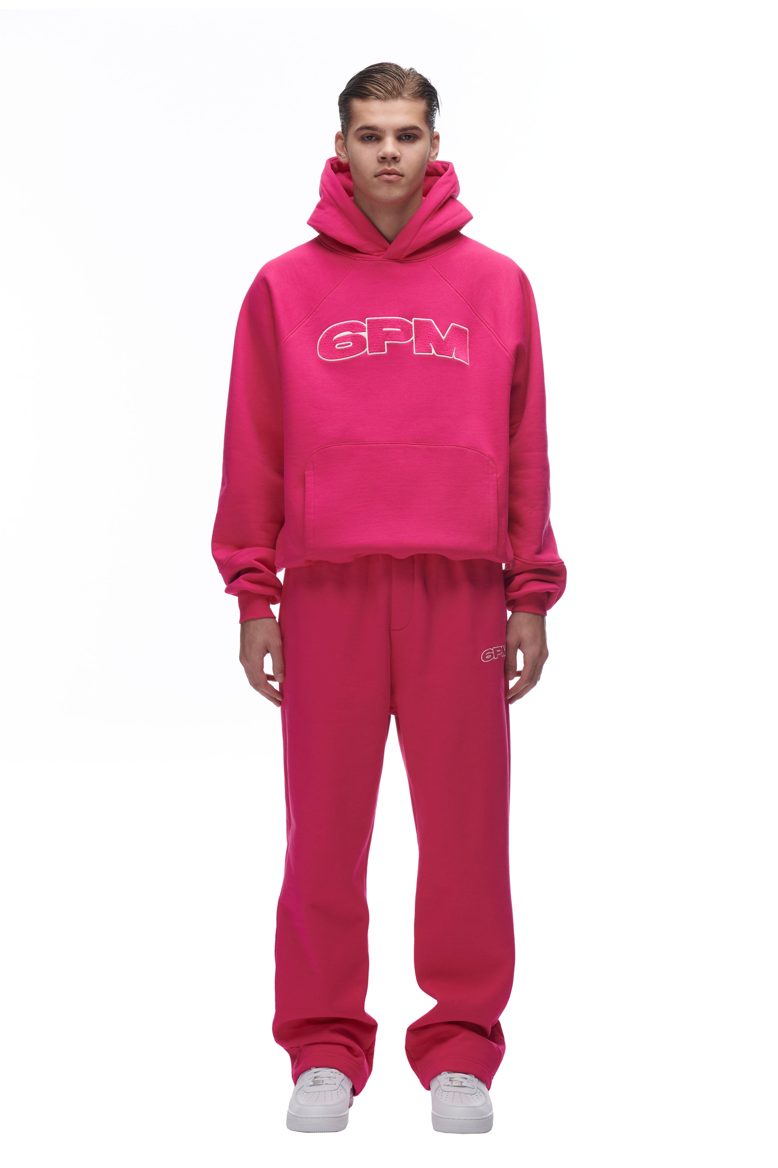 A person faces forward wearing the 6PM LH HOODIE PINK hoodie with matching pink sweatpants and white sneakers, set against a plain white background.