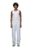 A person with curly hair wears the 6PM TANK TOP WHITE (SINGLE), loose white sweatpants, and white sneakers, standing against a white background.