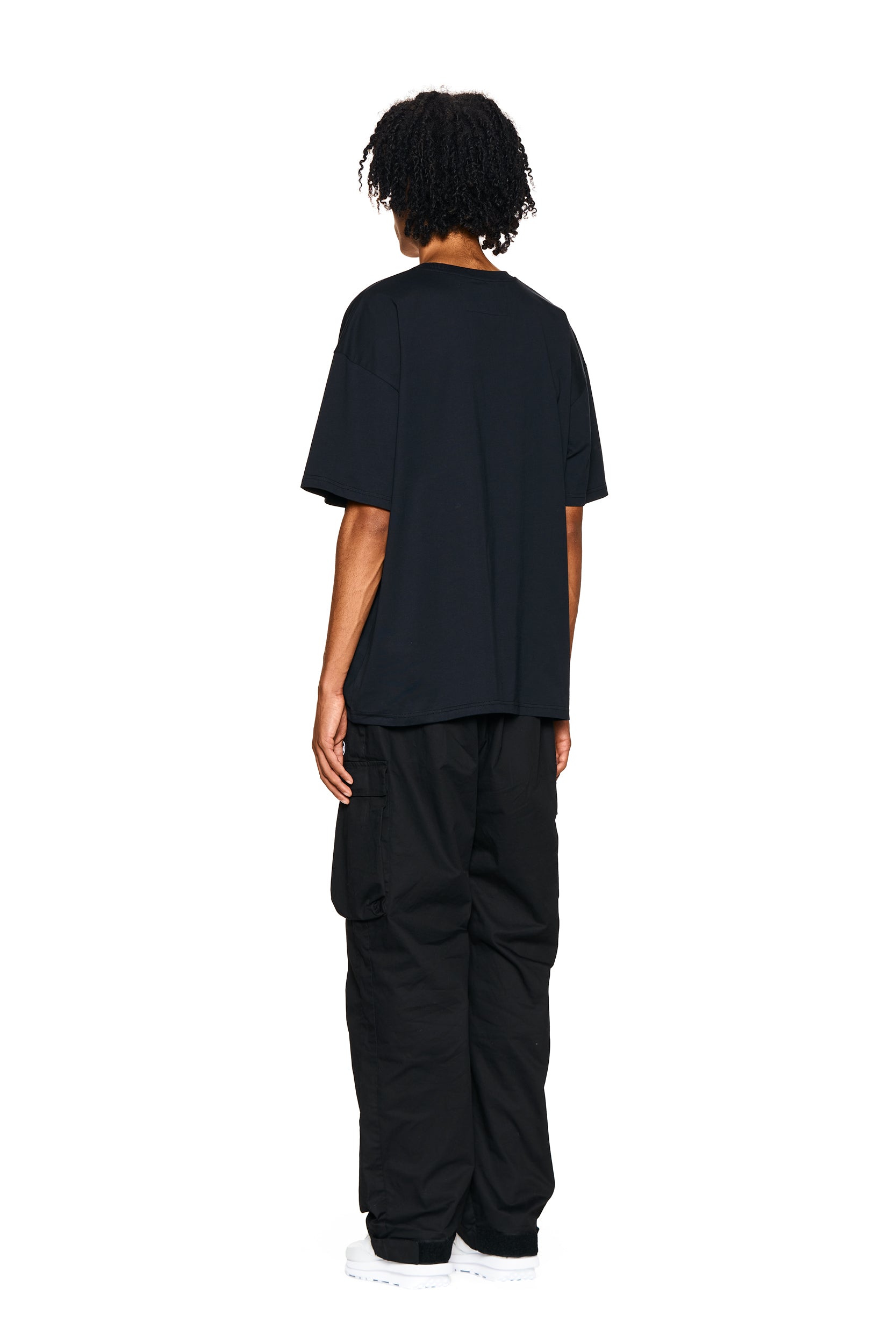 A person with short curly hair faces away from the camera, wearing the 6PM PHONE T-SHIRT BLACK and black cargo pants, set against a plain white background.