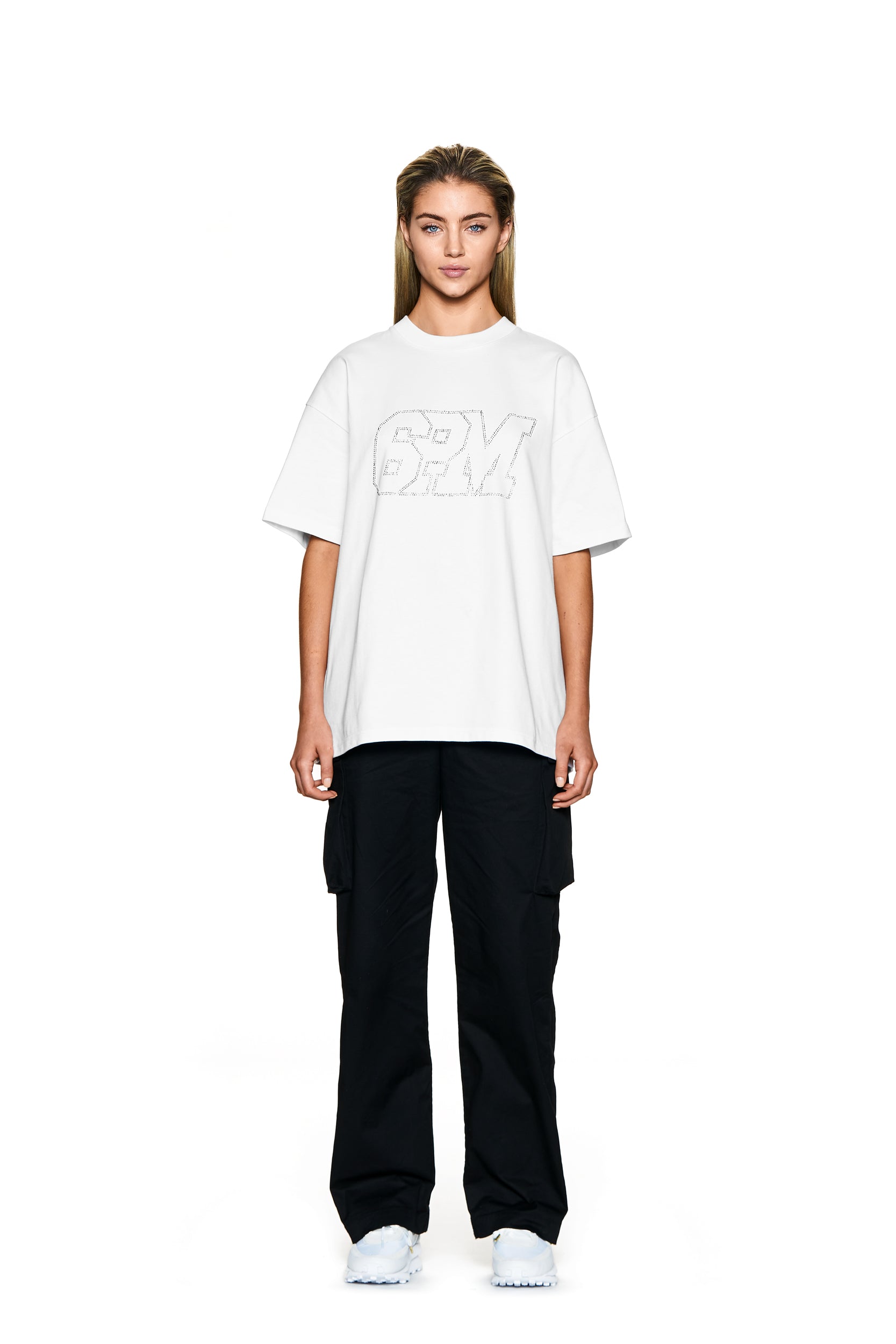 A person stands facing forward against a plain white background, wearing the 6PM BLING T-SHIRT WHITE, black cargo pants, and white sneakers.
