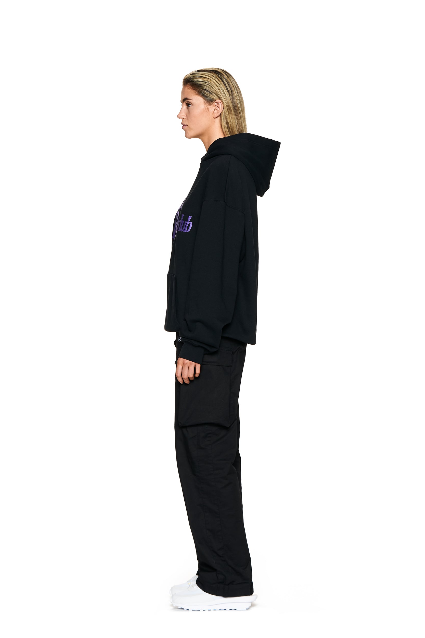 A person with blond hair stands in profile against a white background, wearing the 6PM SAD BOYS HOODIE BLACK, black cargo pants, and white sneakers.