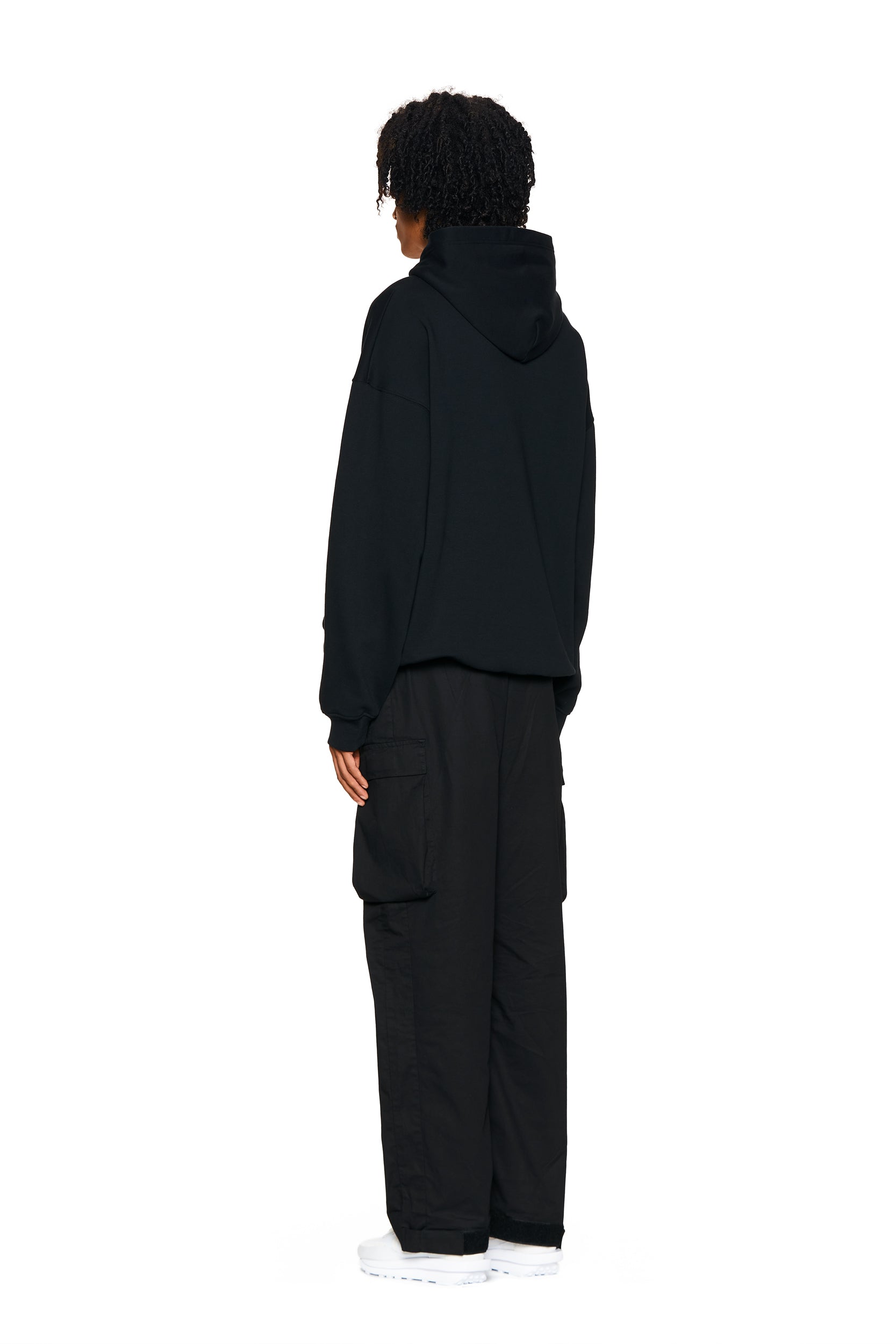 A person with curly hair wears the 6PM LOGO HOODIE BLACK, paired with black cargo pants, facing away at an angle against a plain white background.