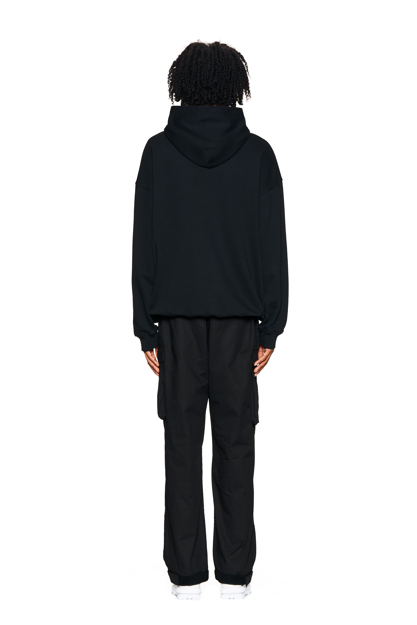 A person with curly hair faces away from the camera, wearing the 6PM LOGO HOODIE BLACK and black cargo pants against a plain white background.