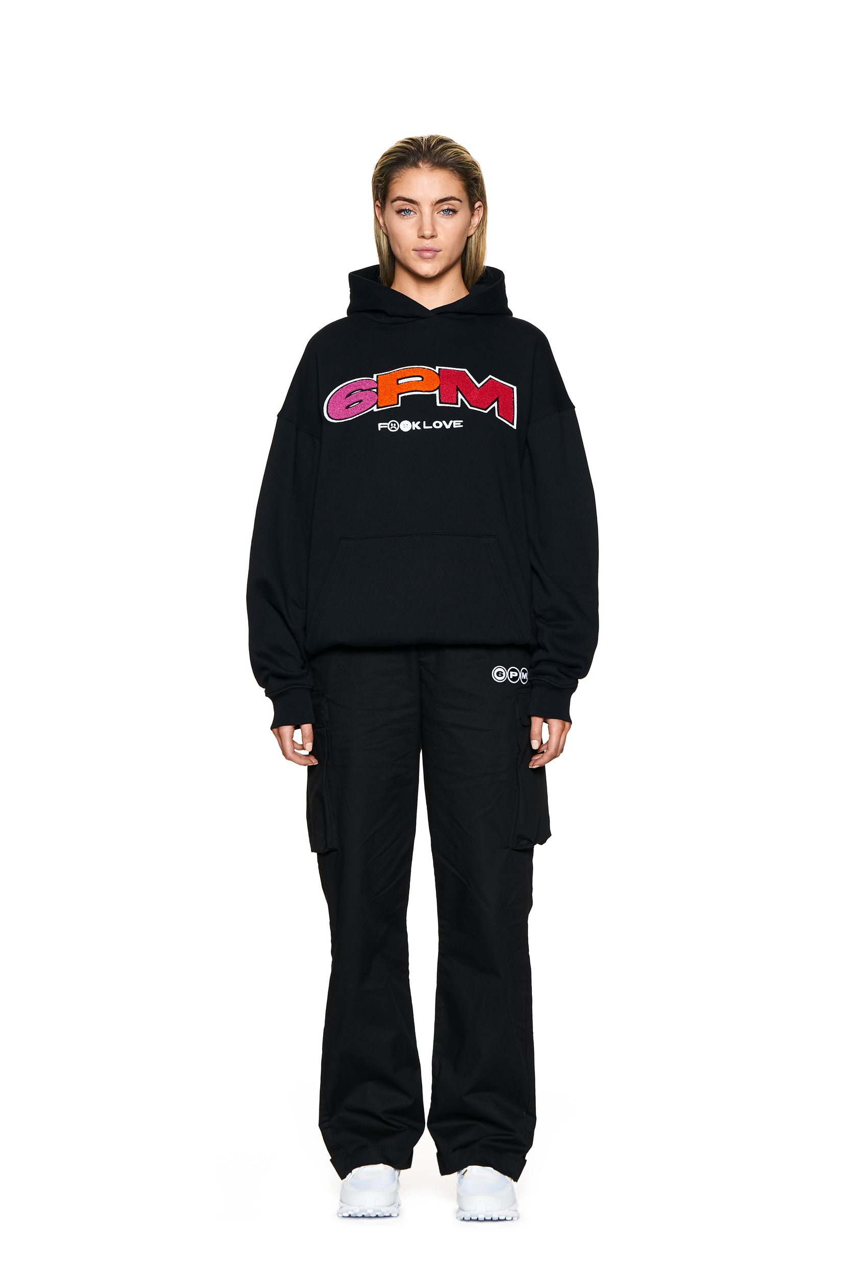 A person faces forward against a white background, wearing the 6PM LOGO HOODIE BLACK, black cargo pants, and white sneakers.