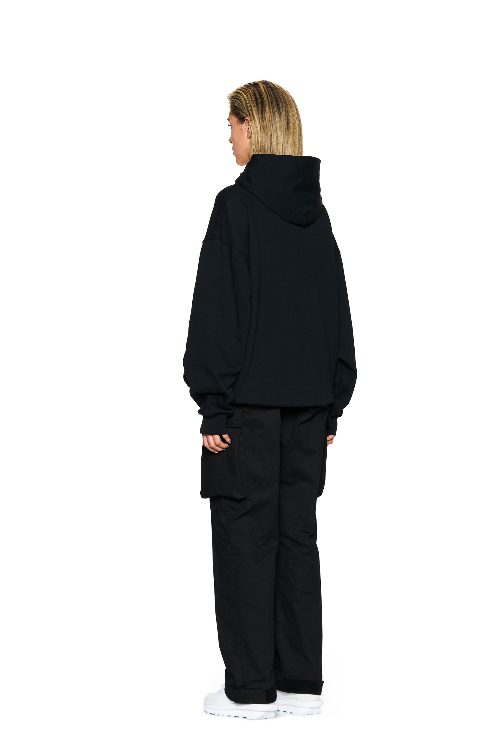 A person with shoulder-length blonde hair faces away, wearing the 6PM FUCK LOVE HOODIE BLACK, black cargo pants, and white sneakers against a plain white background.