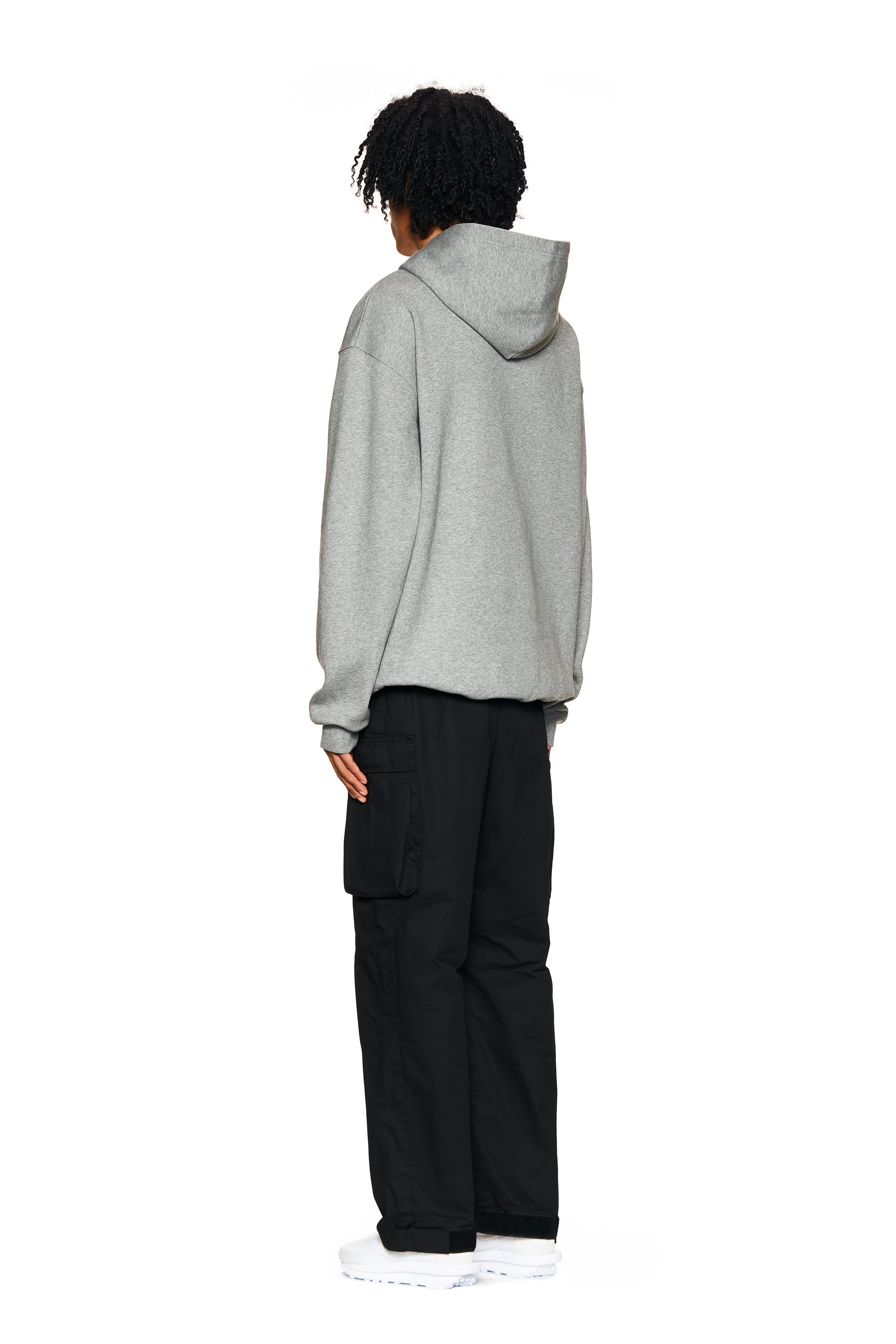 A person stands facing away against a plain white background, wearing the 6PM LOGO HOODIE GREY MELANGE, paired with black cargo pants and white shoes.