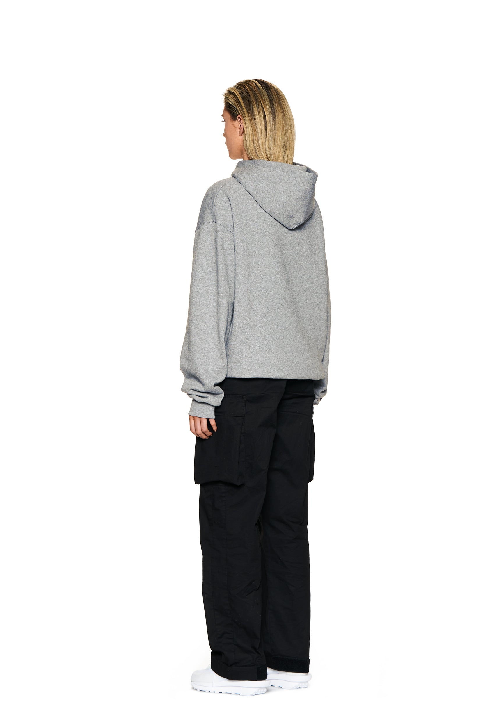 A person stands facing away on a plain white background, wearing the 6PM LOGO HOODIE GREY MELANGE with black cargo pants and white sneakers.
