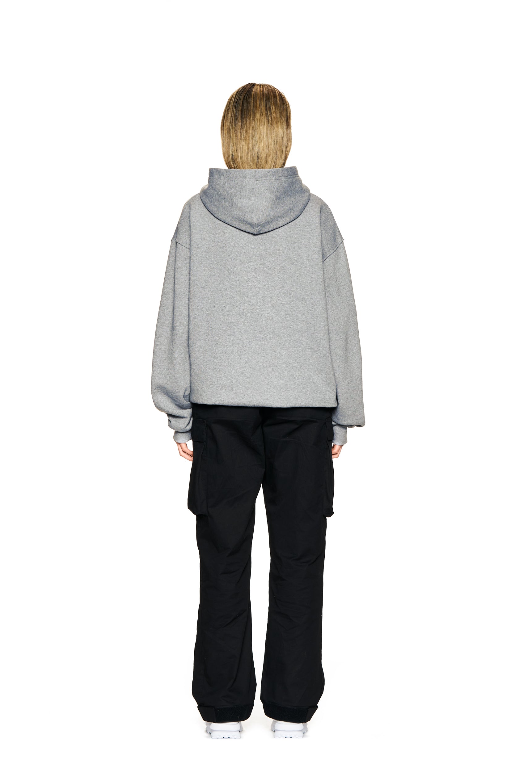 A person with straight, shoulder-length blonde hair faces away against a white background, wearing the 6PM LOGO HOODIE GREY MELANGE, black cargo pants, and white sneakers.
