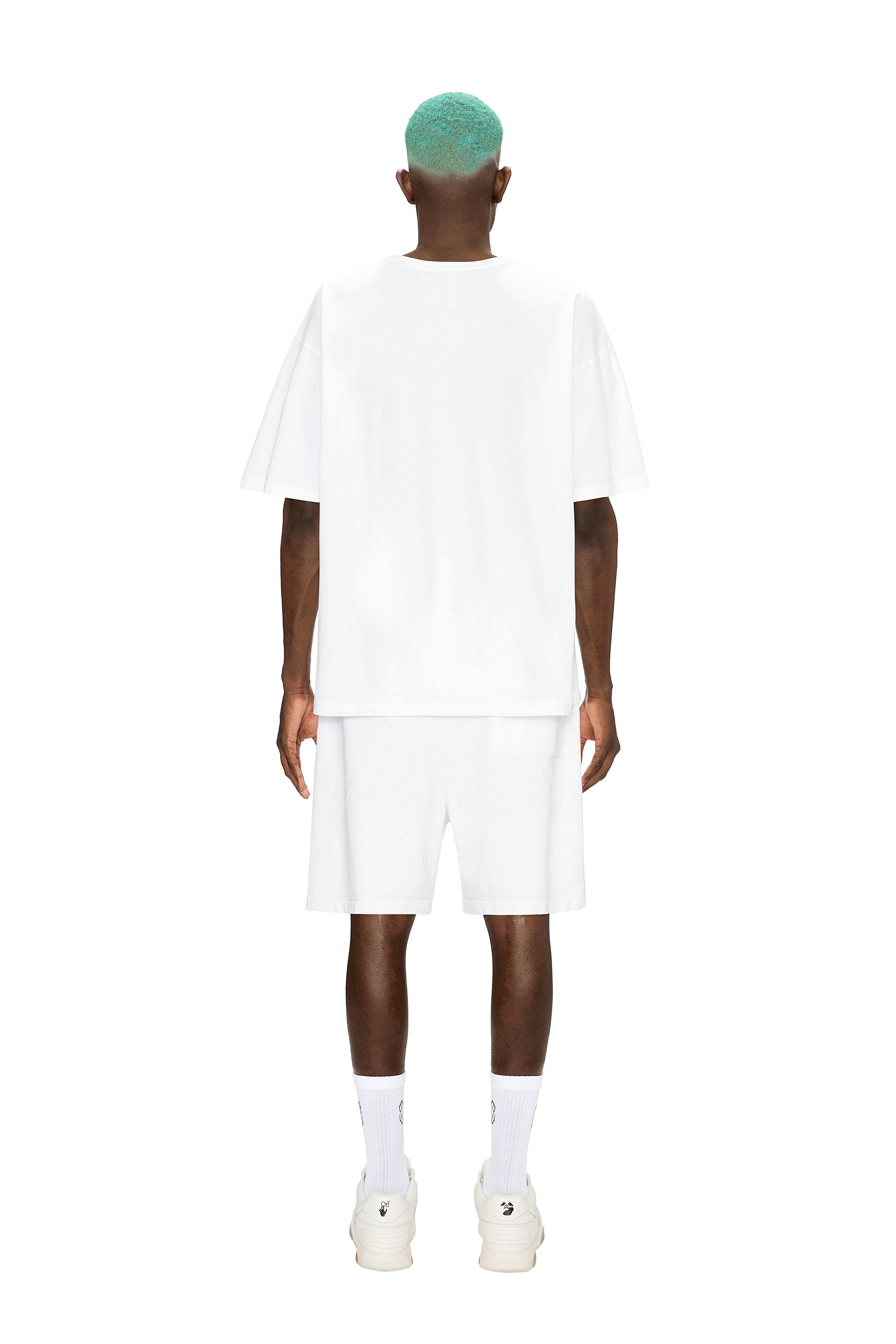 A person with teal hair faces away, wearing the 6PM RAINBOW T-SHIRT WHITE, white shorts, socks, and sneakers against a plain white background.