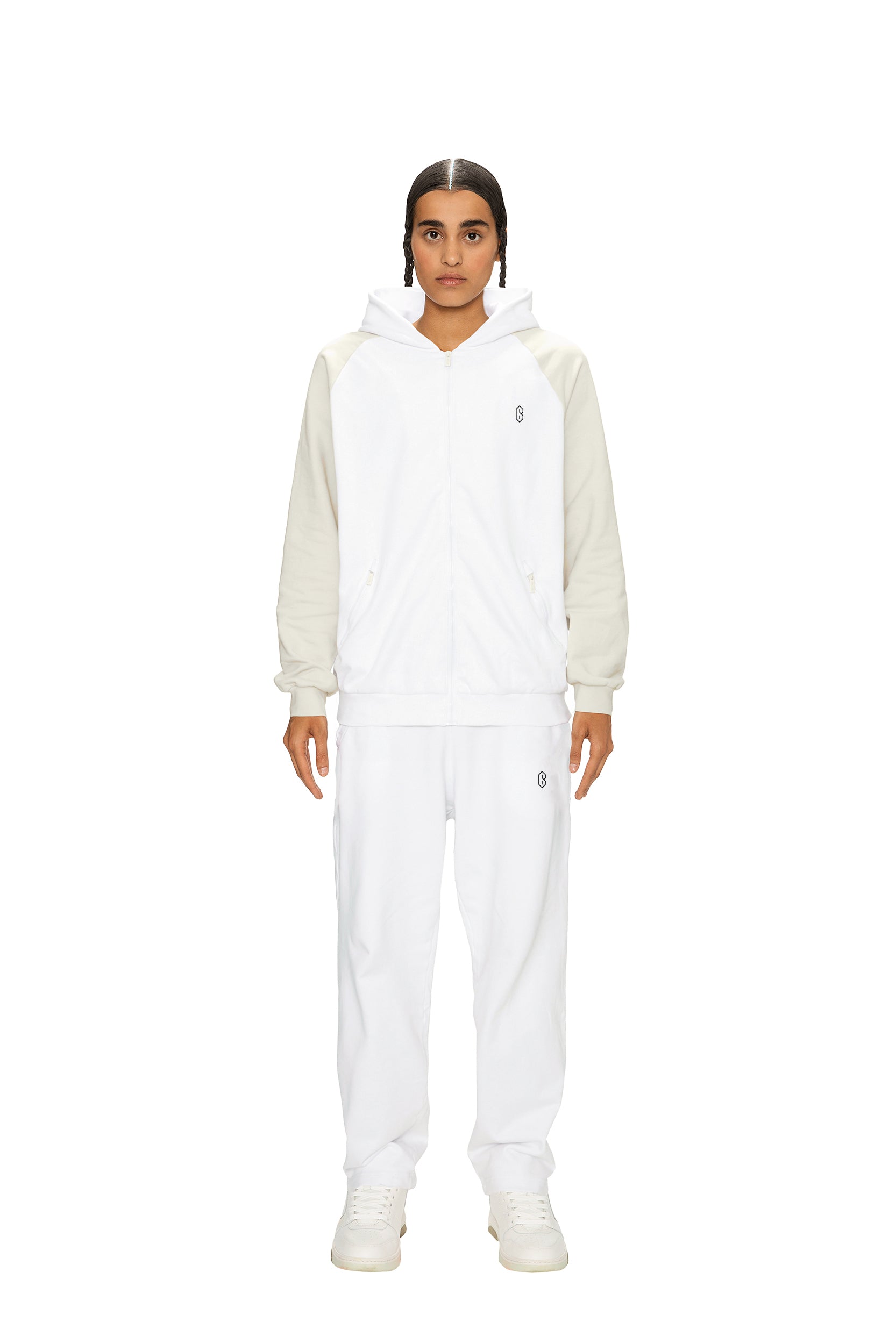 A person stands facing forward in 6PM’s 2-TONE JOGGER WHITE set—white hooded jacket with cream sleeves, matching jogger pants, and white shoes—against a plain white background.