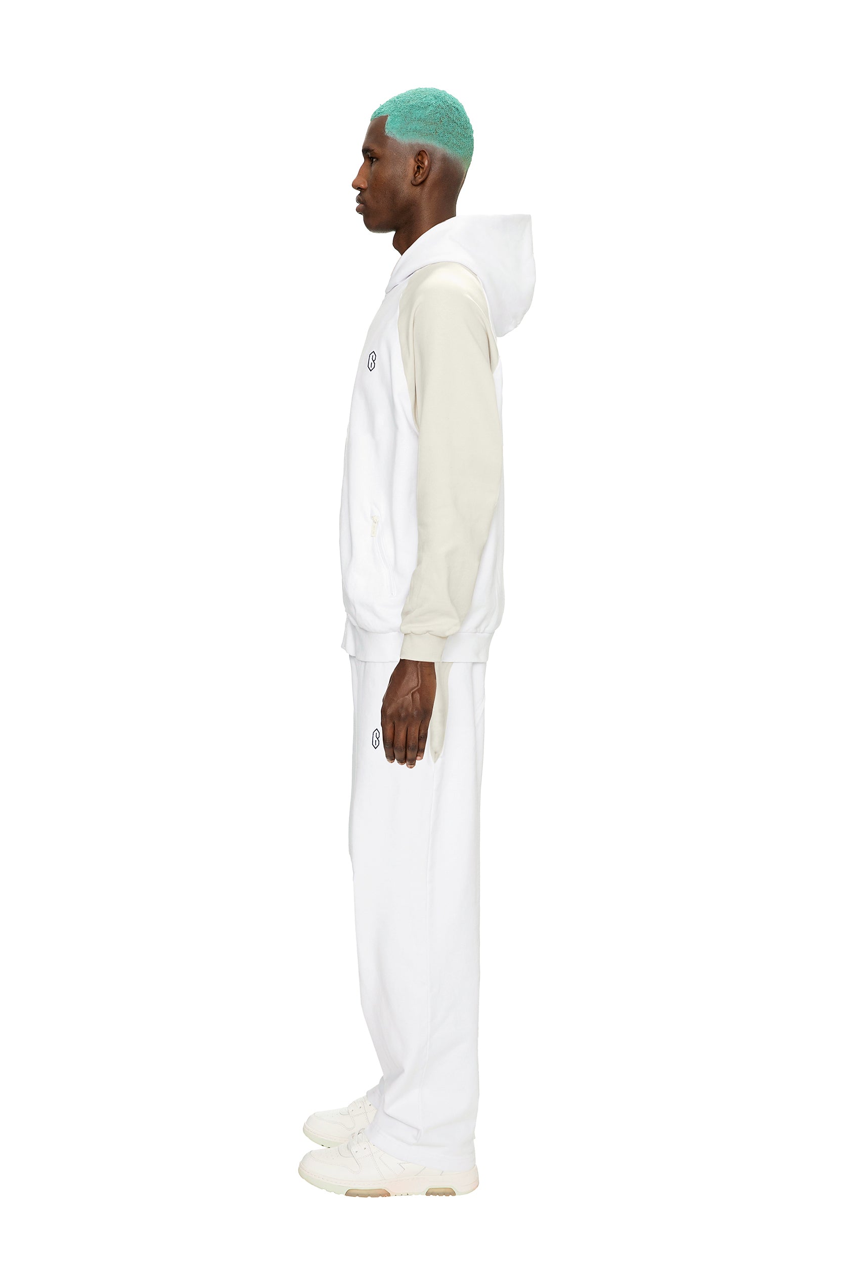 A man with teal hair stands in profile against a white background, wearing the 6PM 2-TONE HOODIE WHITE, paired with white sweatpants and white sneakers.