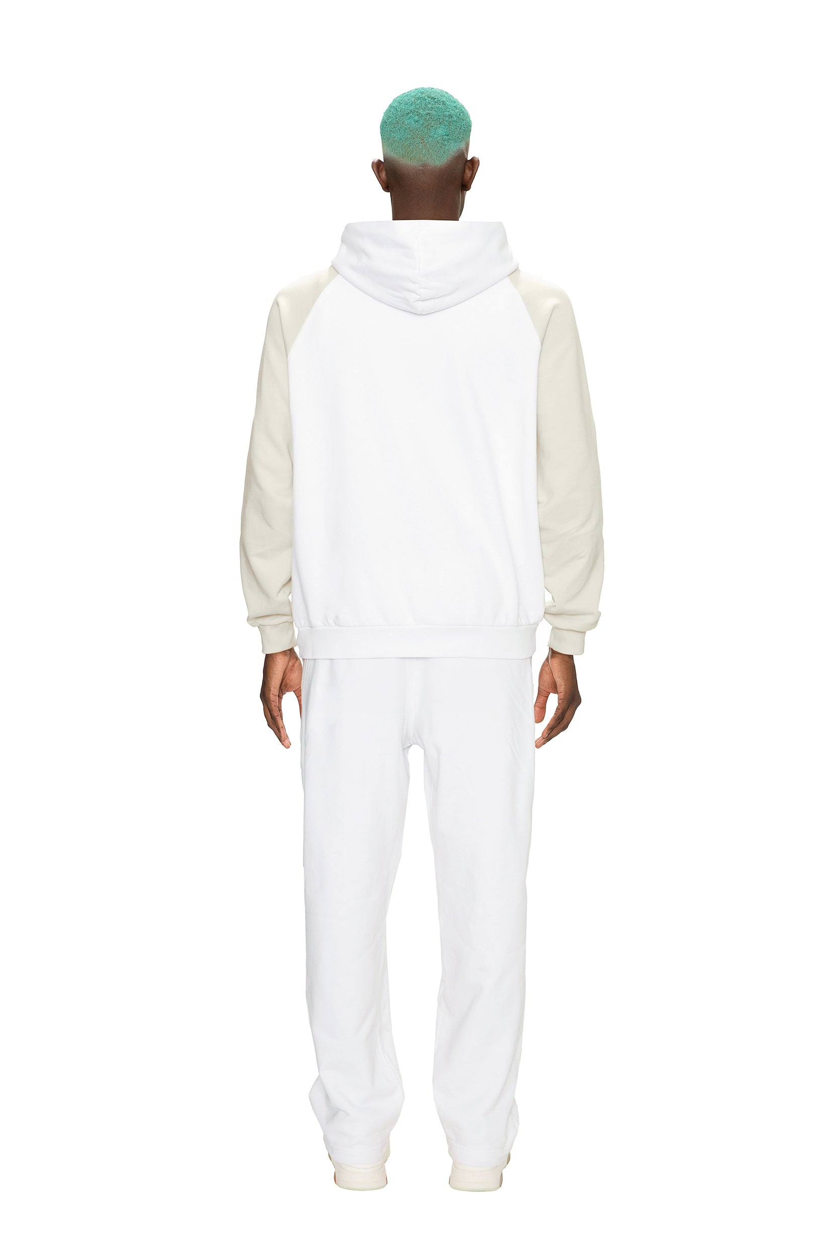A person with teal hair models the 6PM 2-TONE HOODIE WHITE, featuring cream sleeves, paired with white sweatpants, facing away from the camera against a plain white background.
