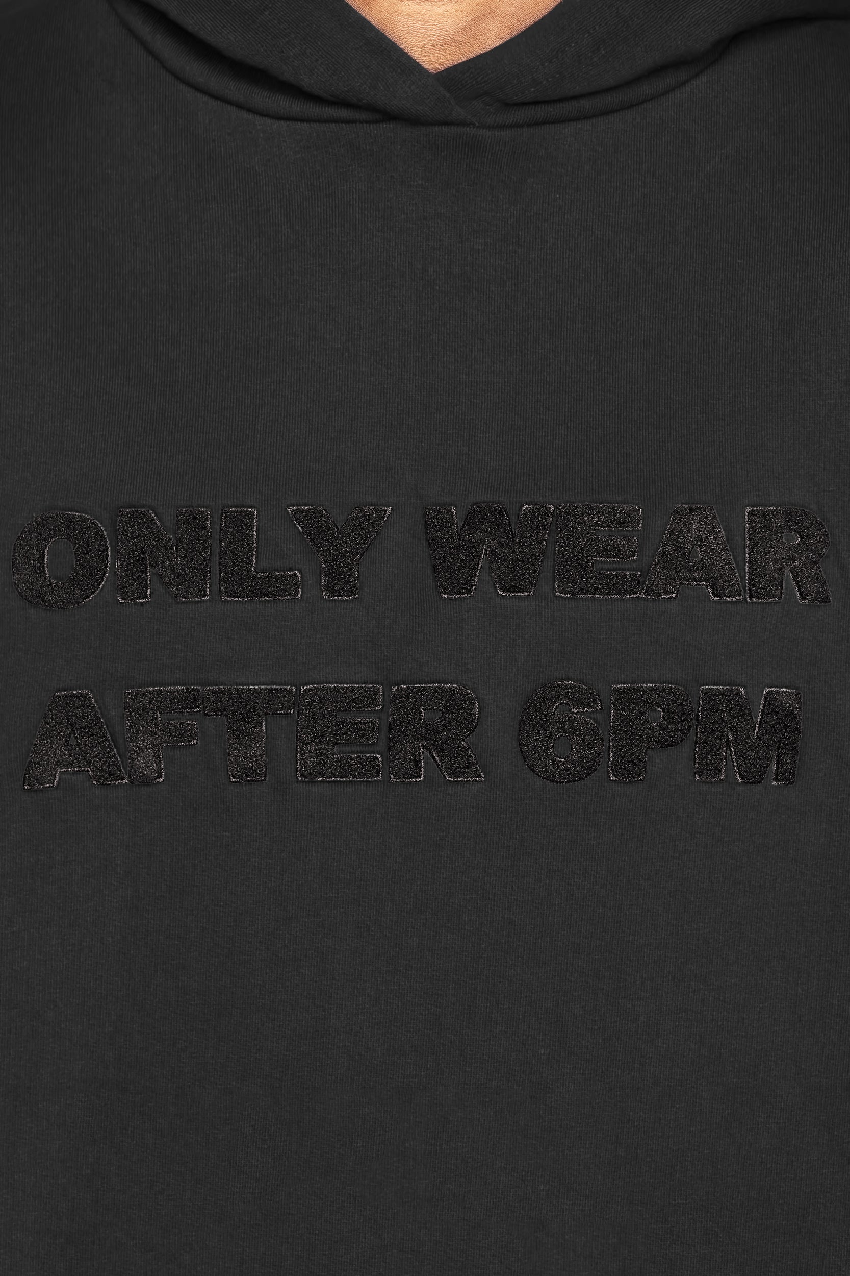 Close-up of the 6PM ONLY WEAR AFTER 6PM HOODIE 2.0 in black, showing its textured black front text and hoodie material on the upper chest area.