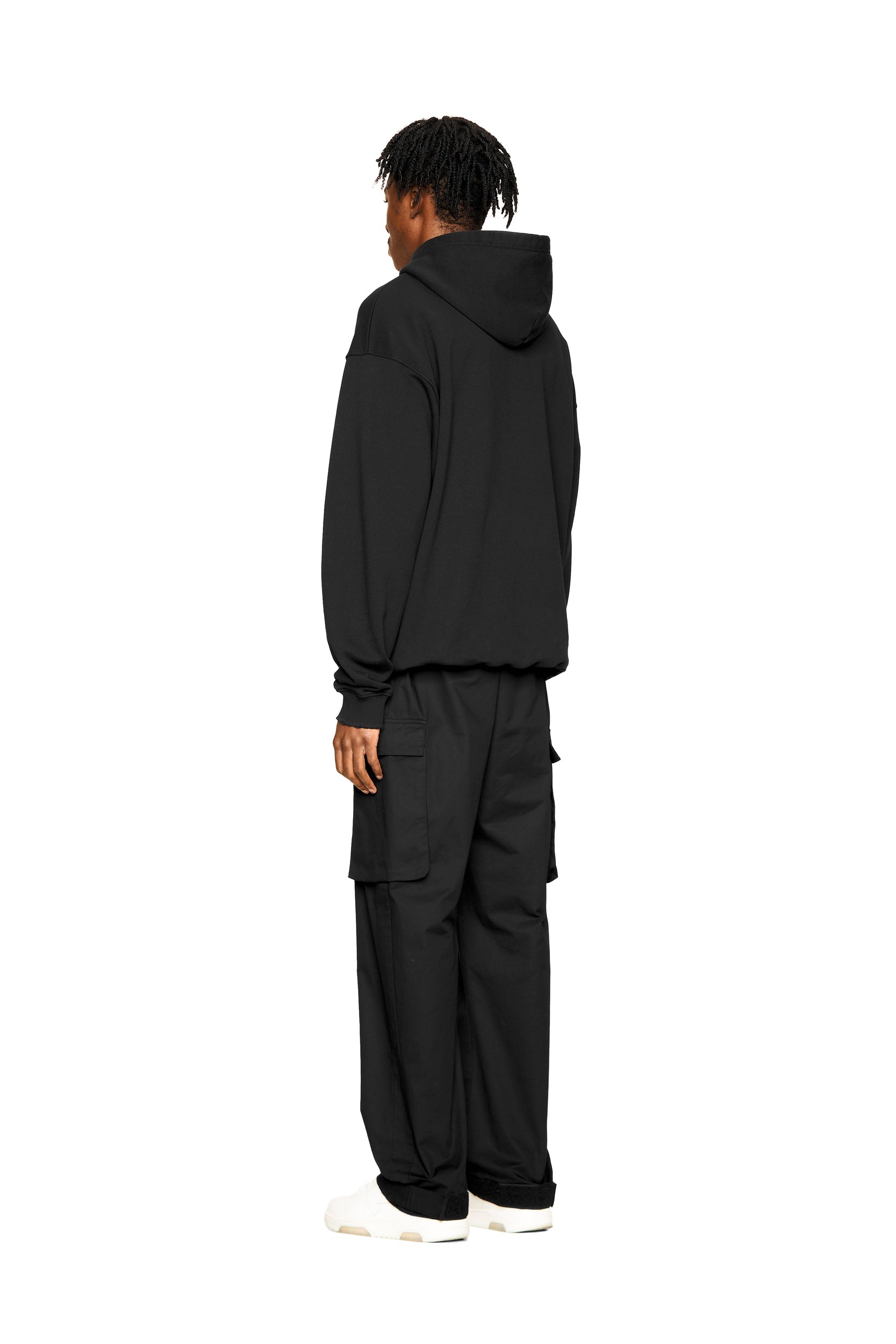 A person stands facing away, wearing the 6PM ONLY WEAR AFTER 6PM HOODIE 2.0 in black with matching black cargo pants and white shoes, set against a clean white background.