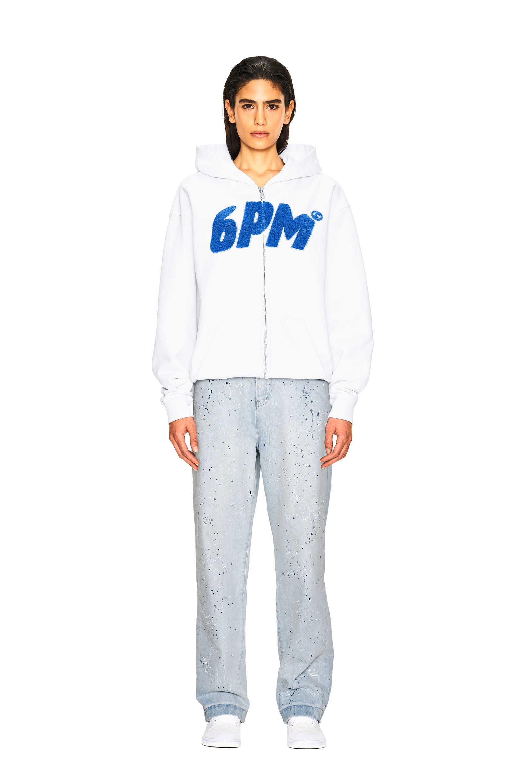 A person stands facing forward in a white 6PM zip-up hoodie and JEANS PANTS BLUE by 6PM, with straight dark hair and white shoes, against a plain white background.