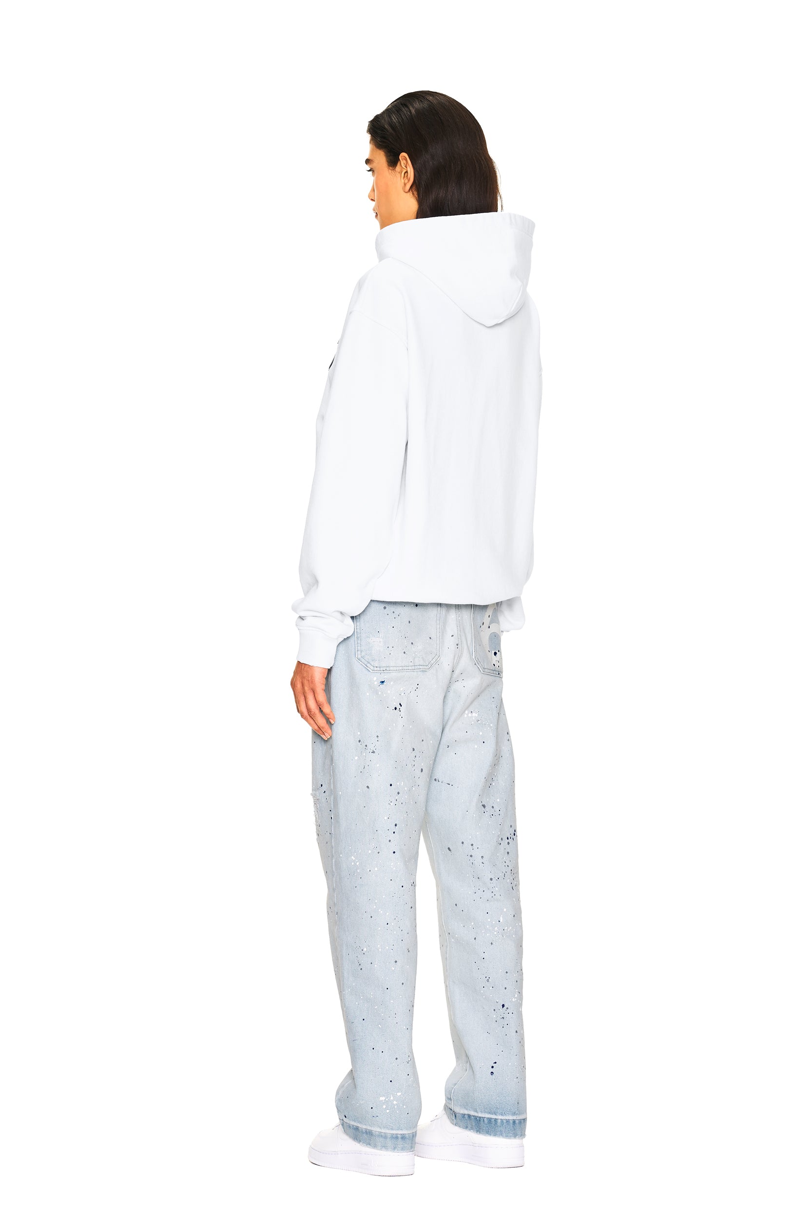 A person faces away, wearing a white hoodie, white sneakers, and 6PM JEANS PANTS BLUE with a paint-splattered design, set against a plain white background.