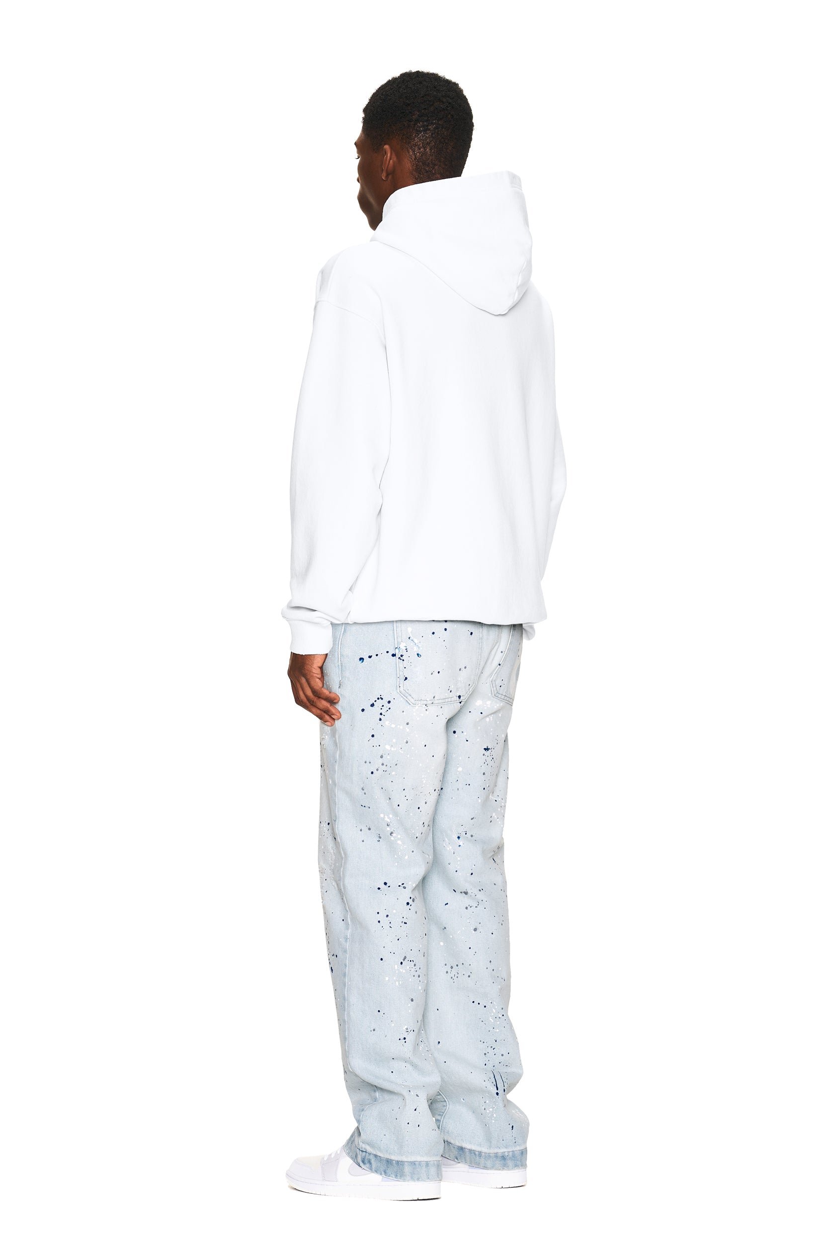 A person stands facing away, wearing the 6PM LOGO ZIP HOODIE WHITE, light blue paint-splattered jeans, and white shoes against a plain white background.