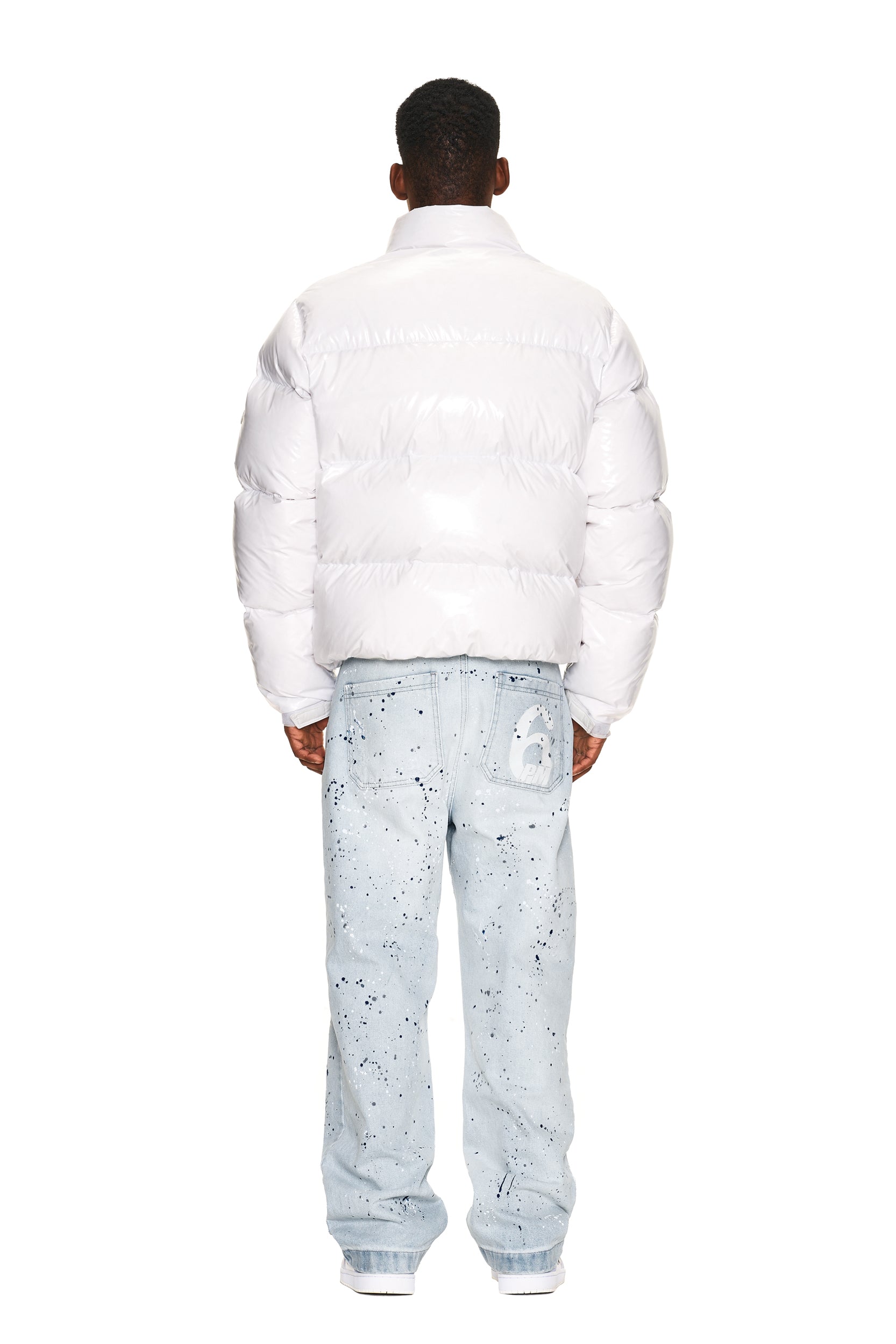 A person faces away in a 6PM DOWN JACKET WHITE SHINY, light blue paint-splattered jeans with a white lock graphic on the back pocket, and white sneakers, all against a plain white background.