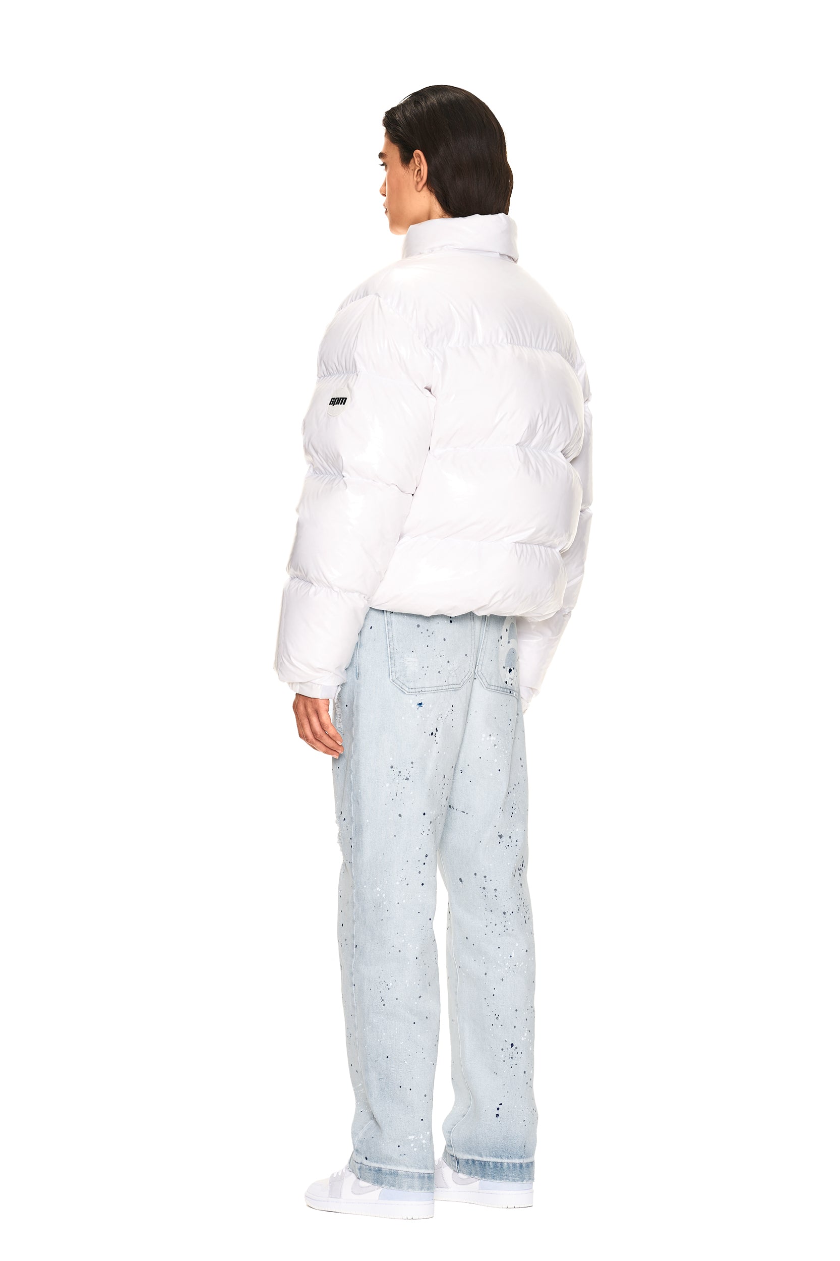 A person faces away against a plain white background, wearing the 6PM DOWN JACKET WHITE SHINY, light blue speckled jeans, and white sneakers.