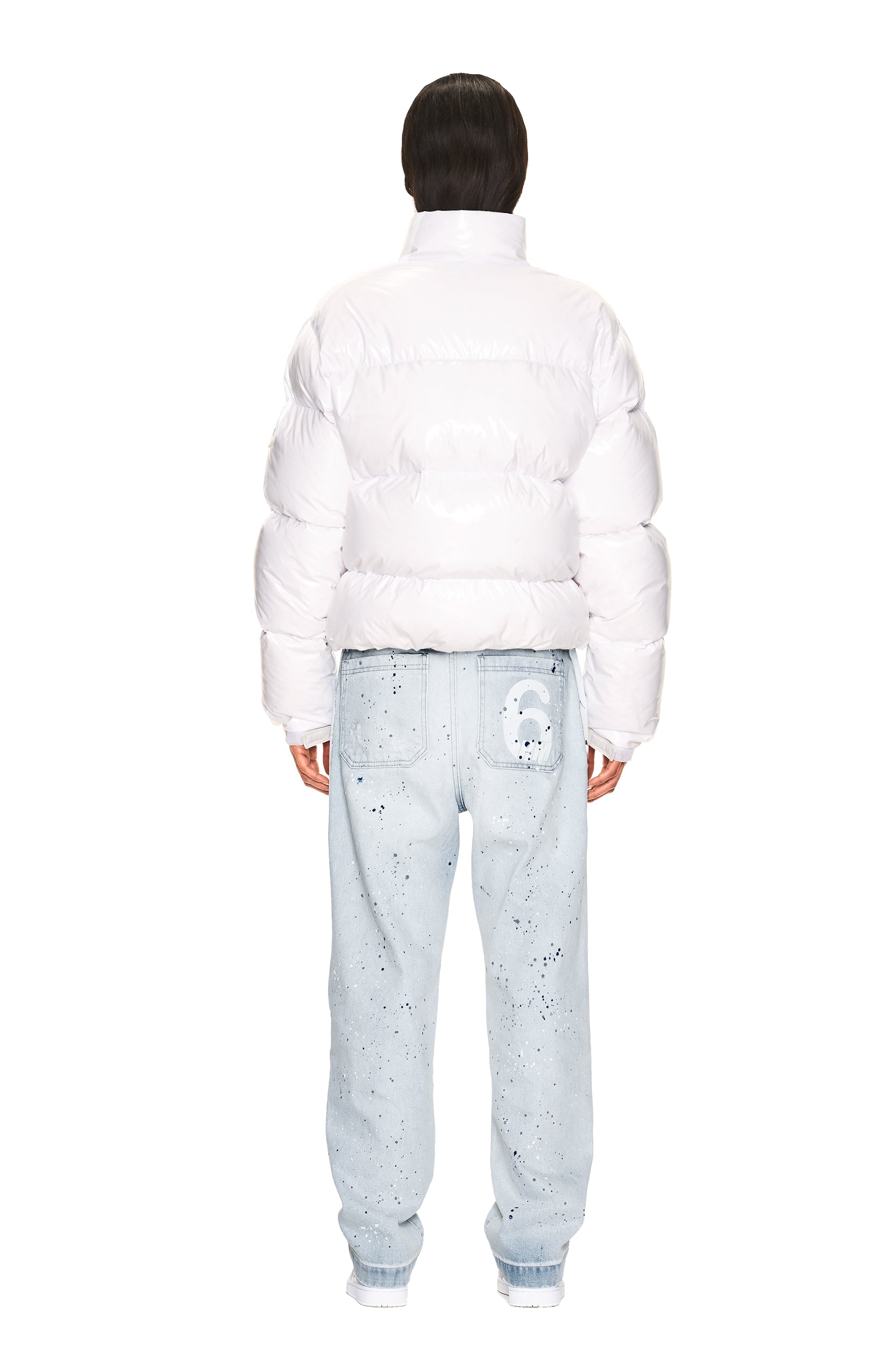 A person stands with their back to the camera, wearing the 6PM DOWN JACKET WHITE SHINY and light blue, paint-splattered jeans with a white graphic on one back pocket, set against a plain white background.