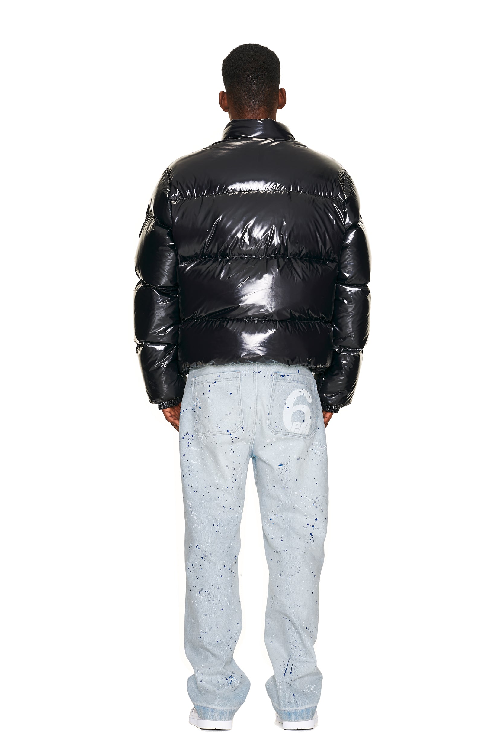 A person faces away in a 6PM DOWN JACKET BLACK SHINY and light blue jeans with paint splatters and a large white number 6 on the back pocket, set against a plain white background.