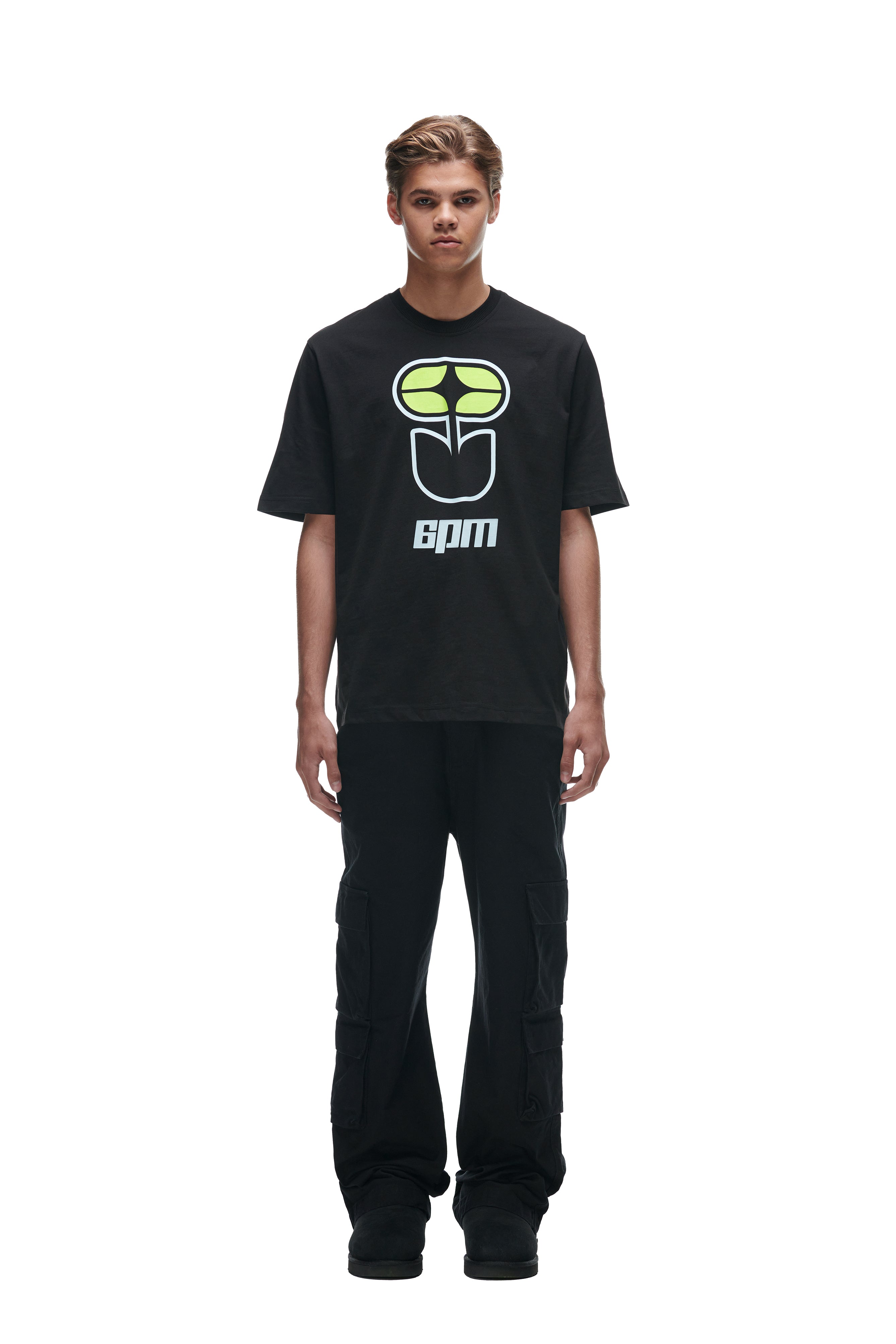 A young person faces forward against a white background, wearing the 6PM FLOWER TSHIRT BLACK, black cargo pants, and black shoes.
