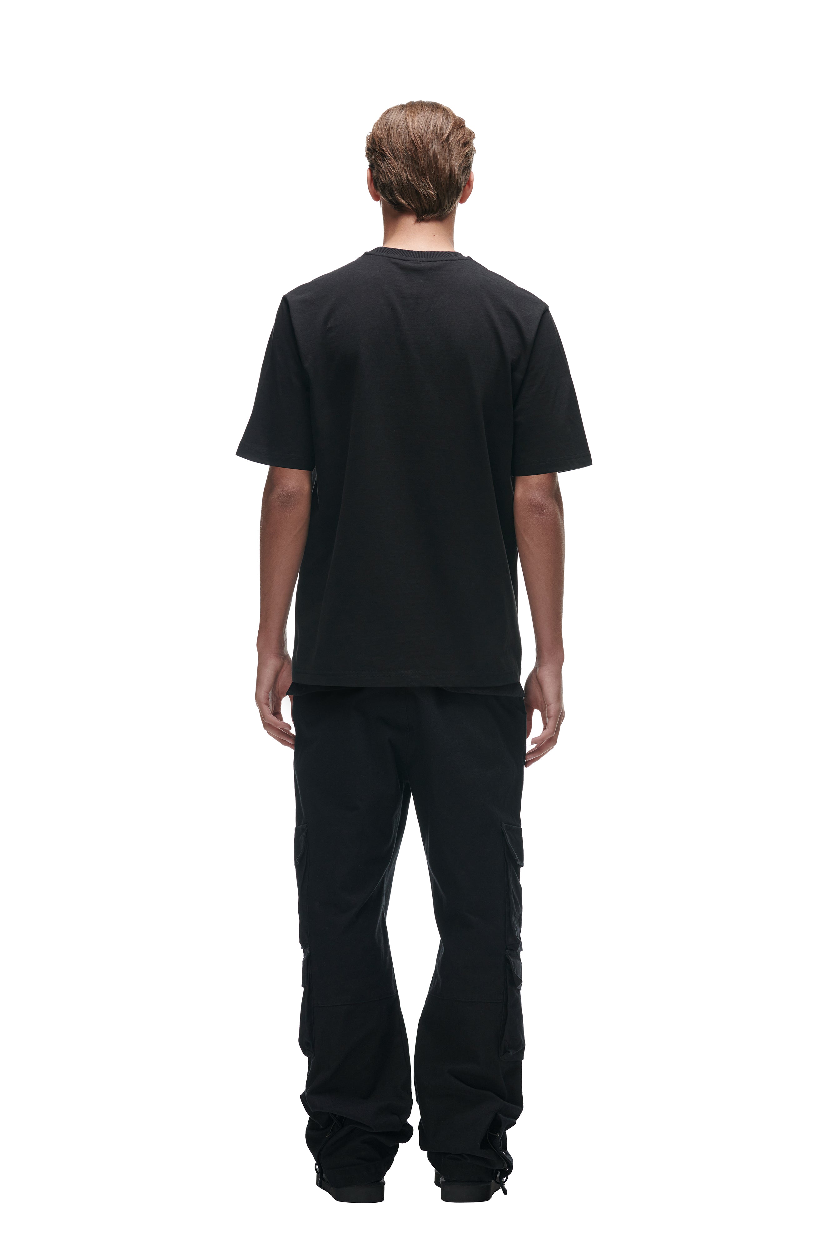A person stands facing away, wearing the 6PM FLOWER TSHIRT BLACK, black cargo pants, and black shoes against a white background.