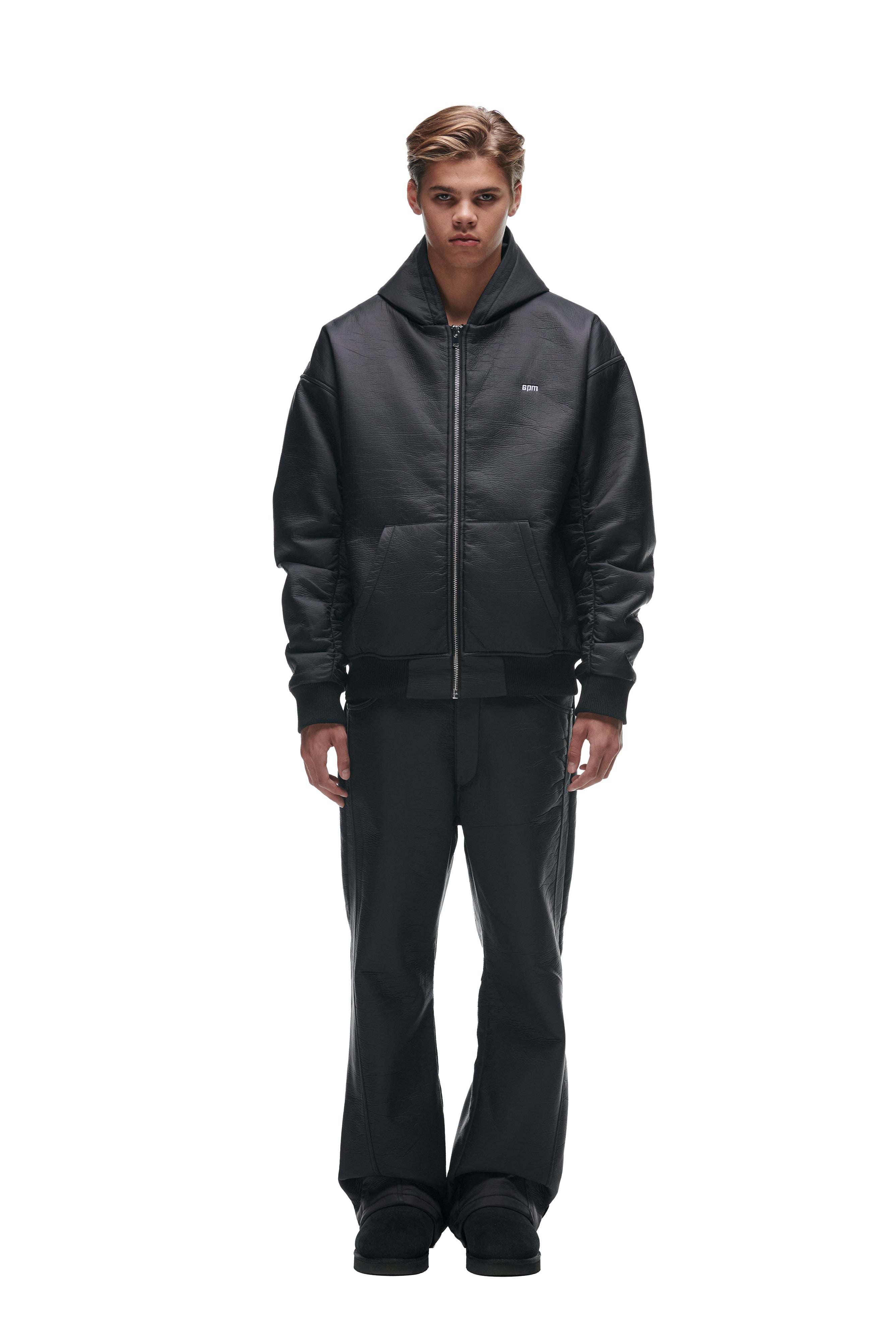 A person stands facing forward in a white background, wearing the 6PM CRINKLE ZIP JACKET BLACK, paired with black pants and black shoes, highlighting the sleek all-black outfit.