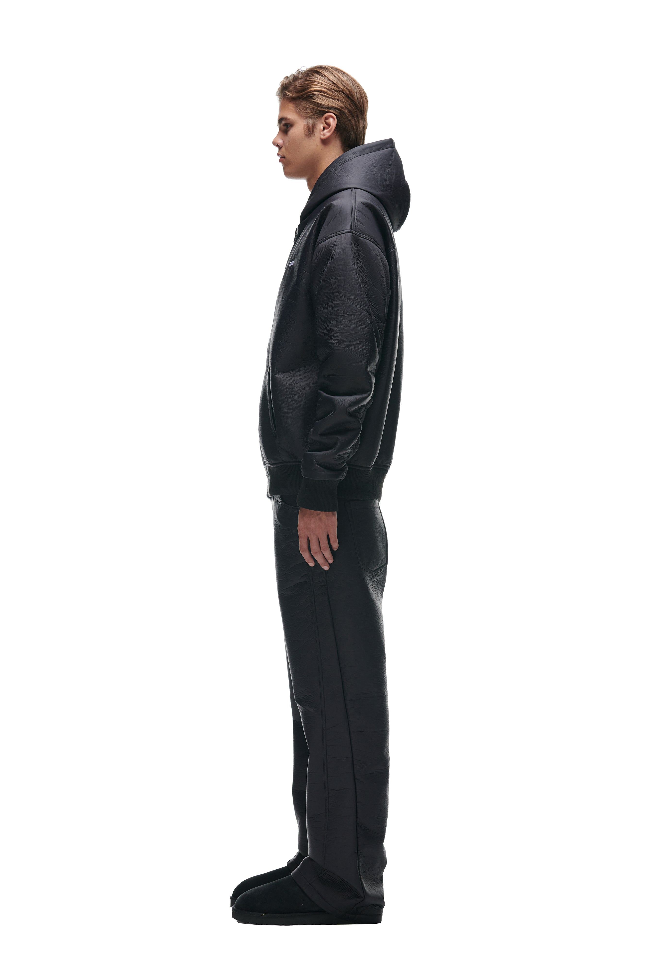 A young person stands in profile facing left, wearing the 6PM CRINKLE ZIP JACKET BLACK, with matching black pants and black footwear, against a plain white background.