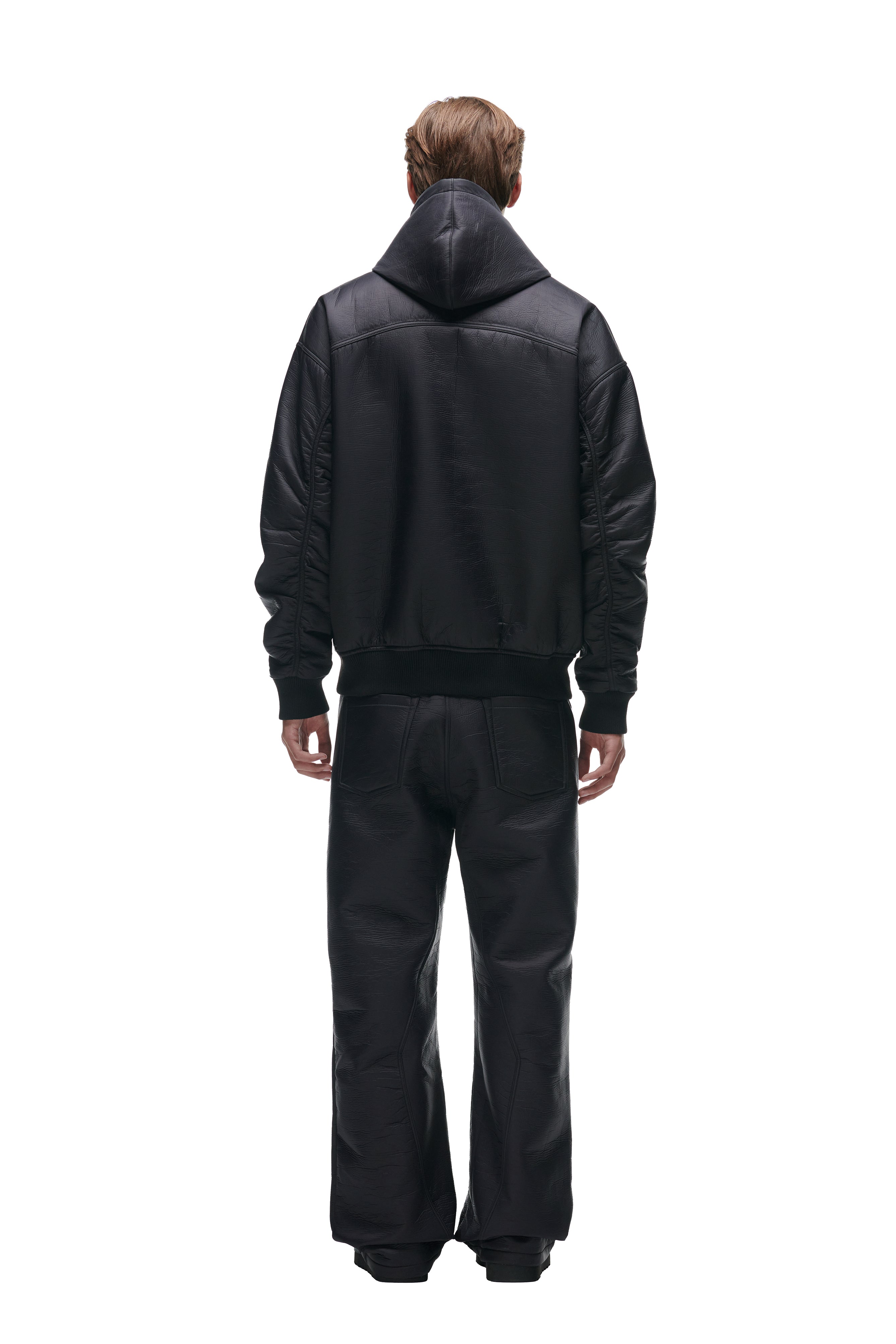 A person stands facing away, wearing the 6PM CRINKLE ZIP JACKET BLACK with a hood and matching black leather pants against a plain white background.