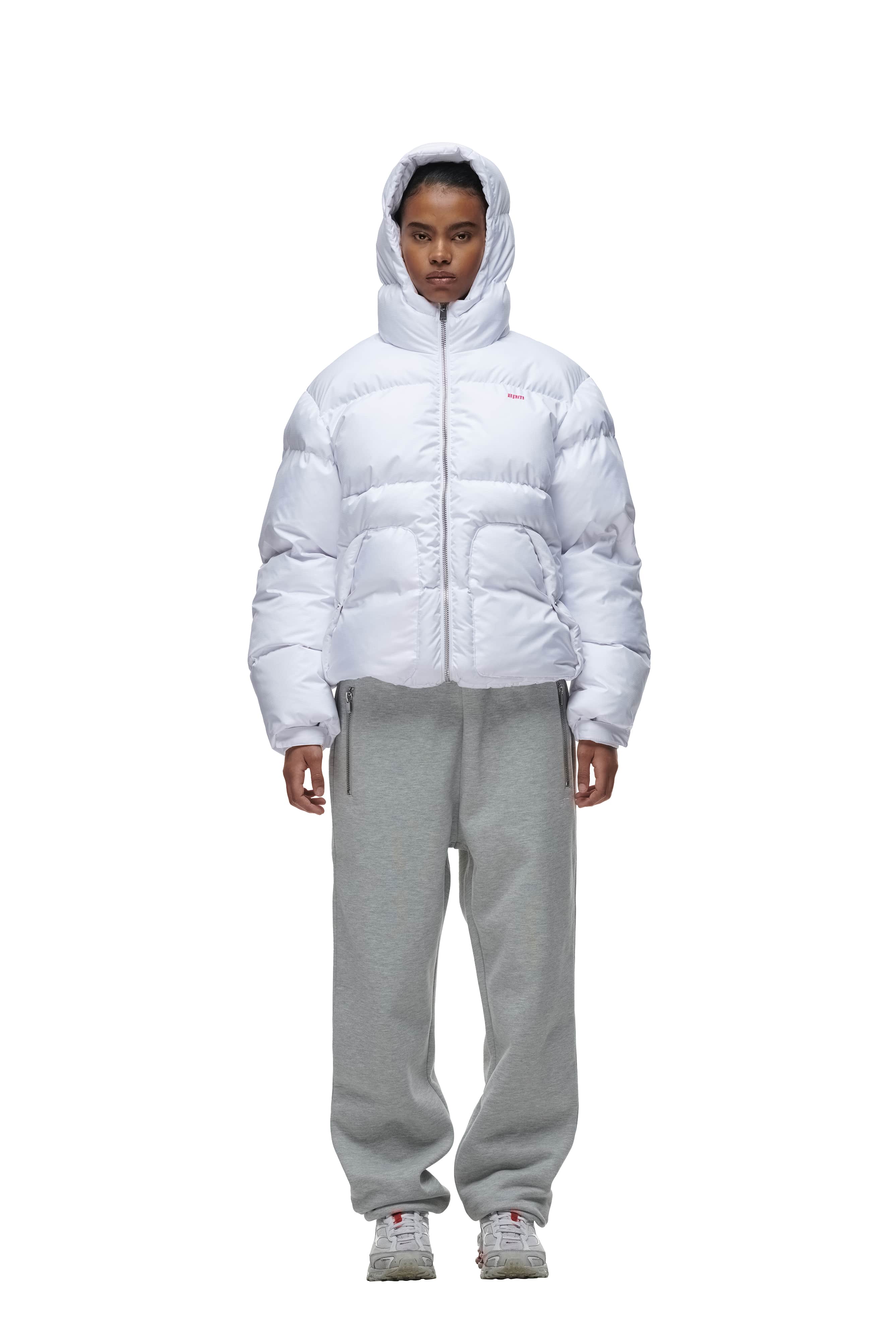 A person stands facing forward wearing the 6PM PUFFER JACKET WHITE with the hood up, paired with gray sweatpants and gray sneakers against a plain white background.