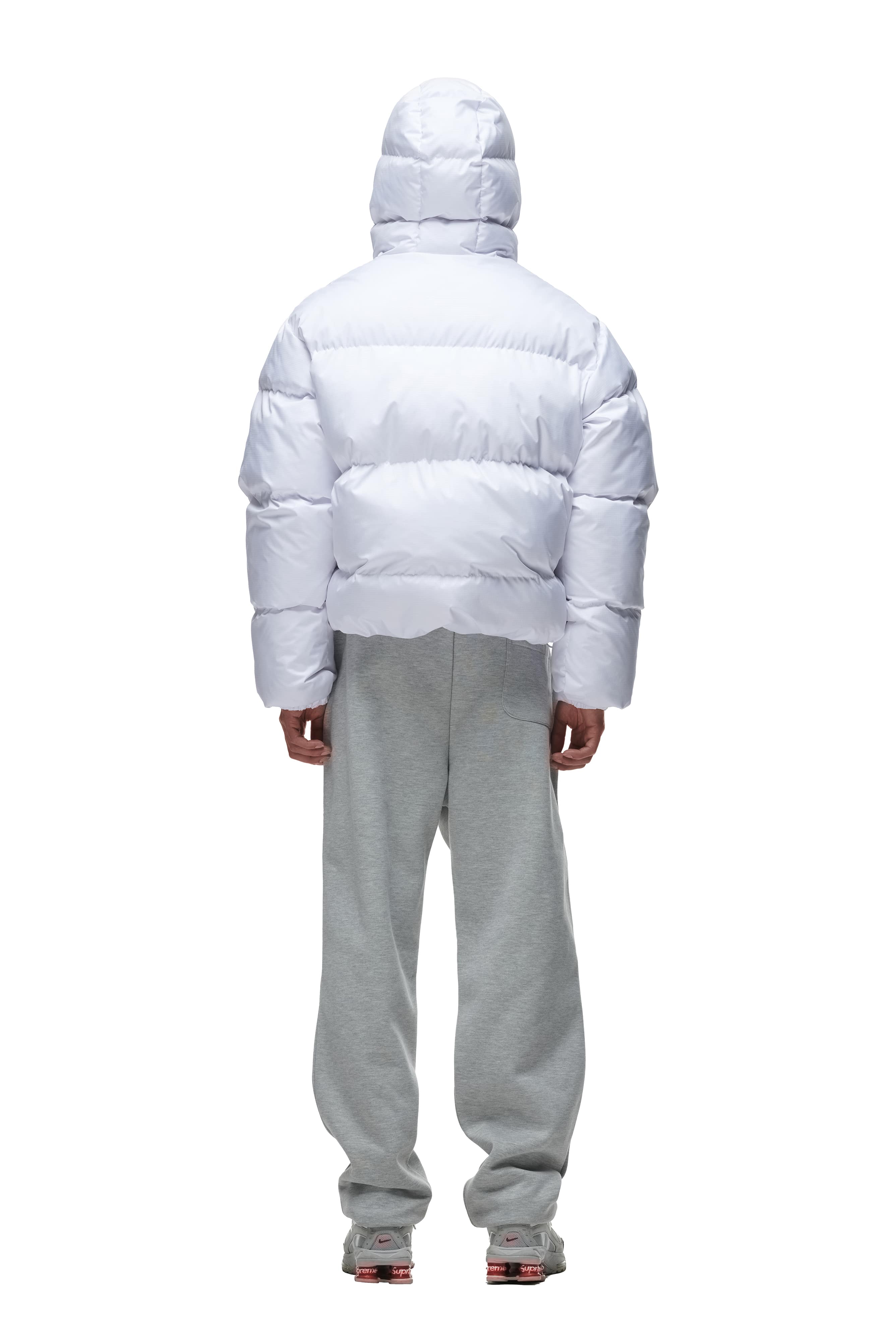 A person stands facing away, wearing the 6PM PUFFER JACKET WHITE with a hood and light gray sweatpants against a plain white background.