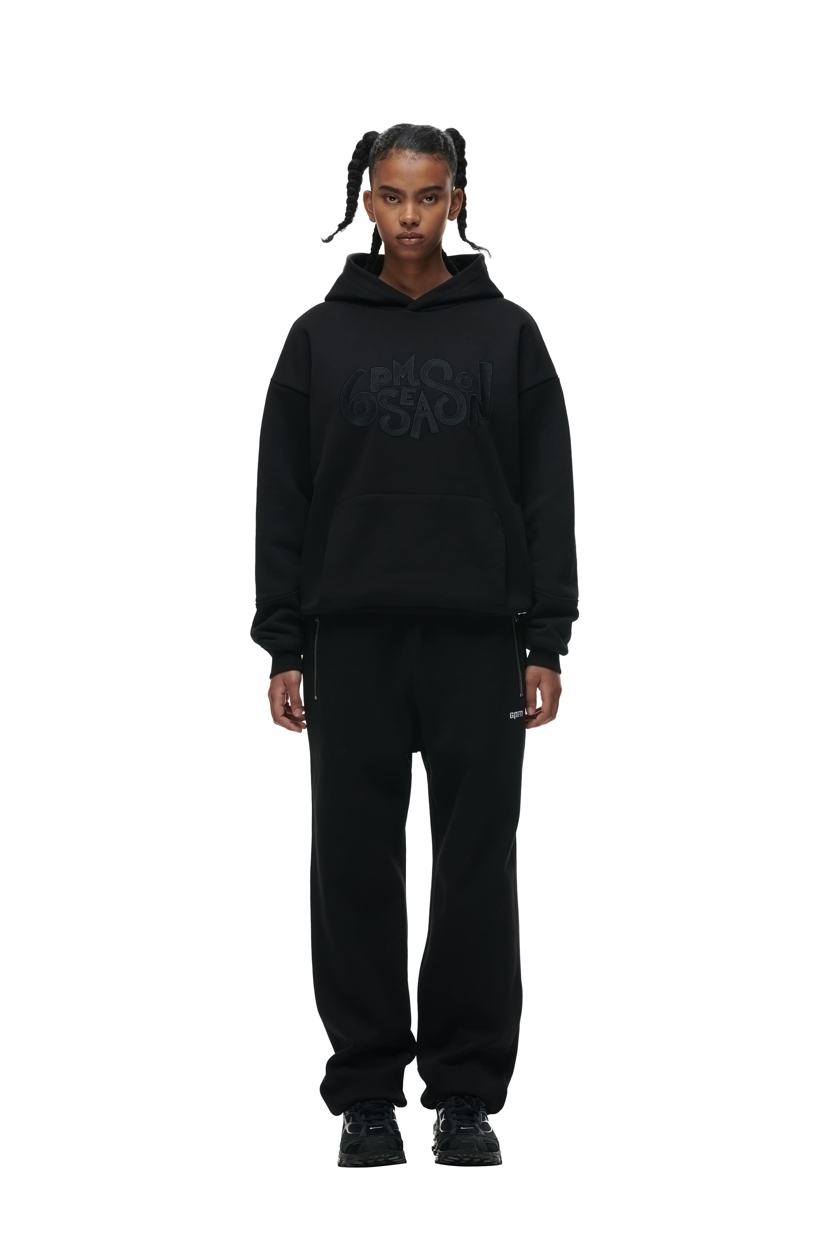 A person with braided hair wears the 6PM DOUBLE LAYER PLAY HOODIE BLACK, paired with black sweatpants and sneakers, standing against a plain white background.