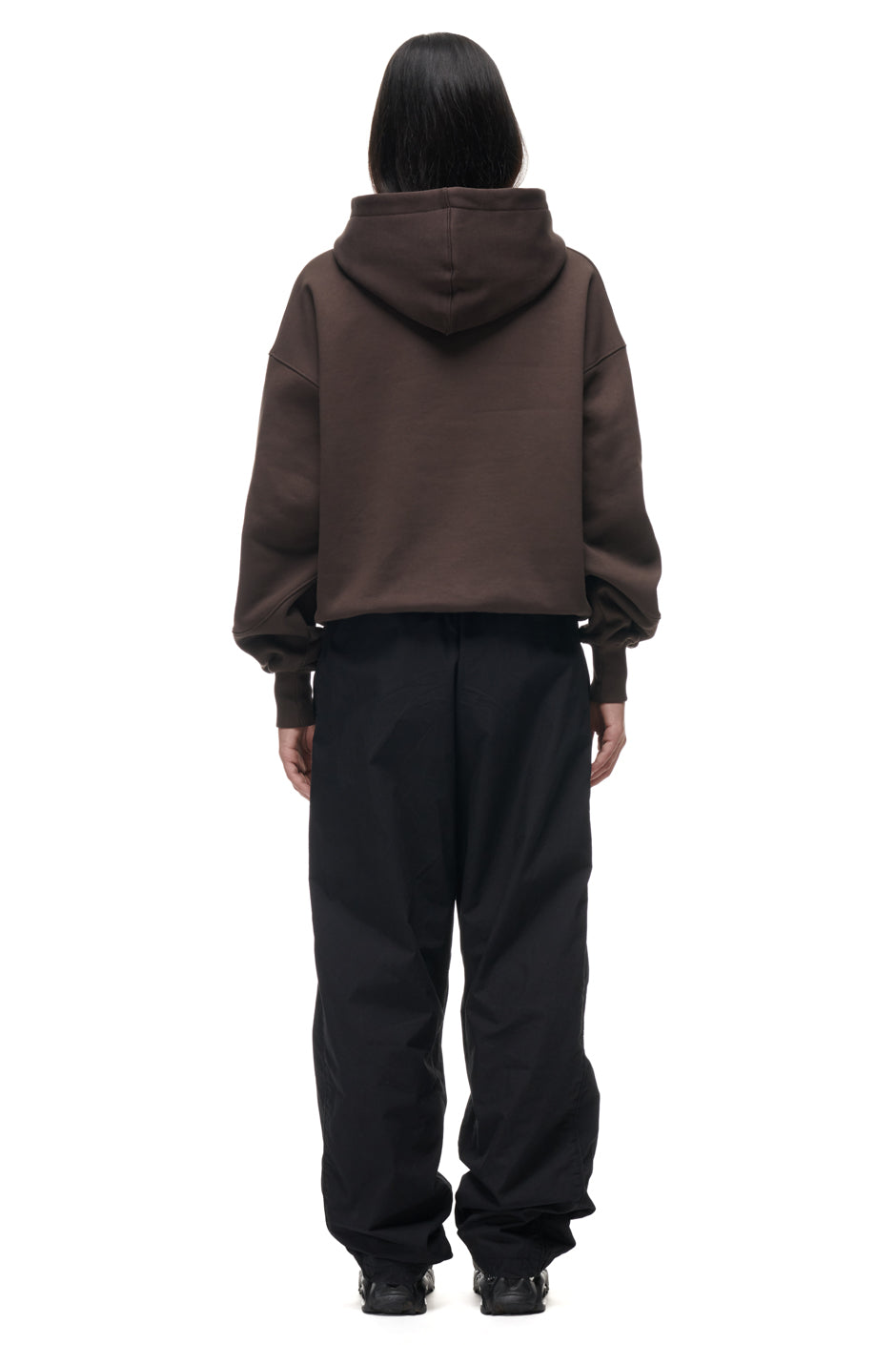 A person stands facing away against a plain white background, wearing the 6PM TILES HOODIE BROWN and loose black pants.