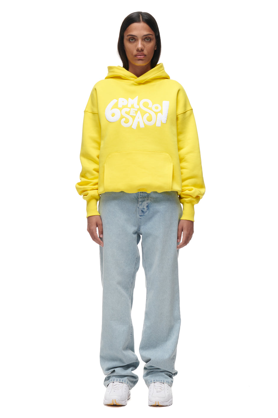 A person faces forward wearing the 6PM PLAY HOODIE YELLOW, styled with light blue jeans and white sneakers, set against a plain white background.