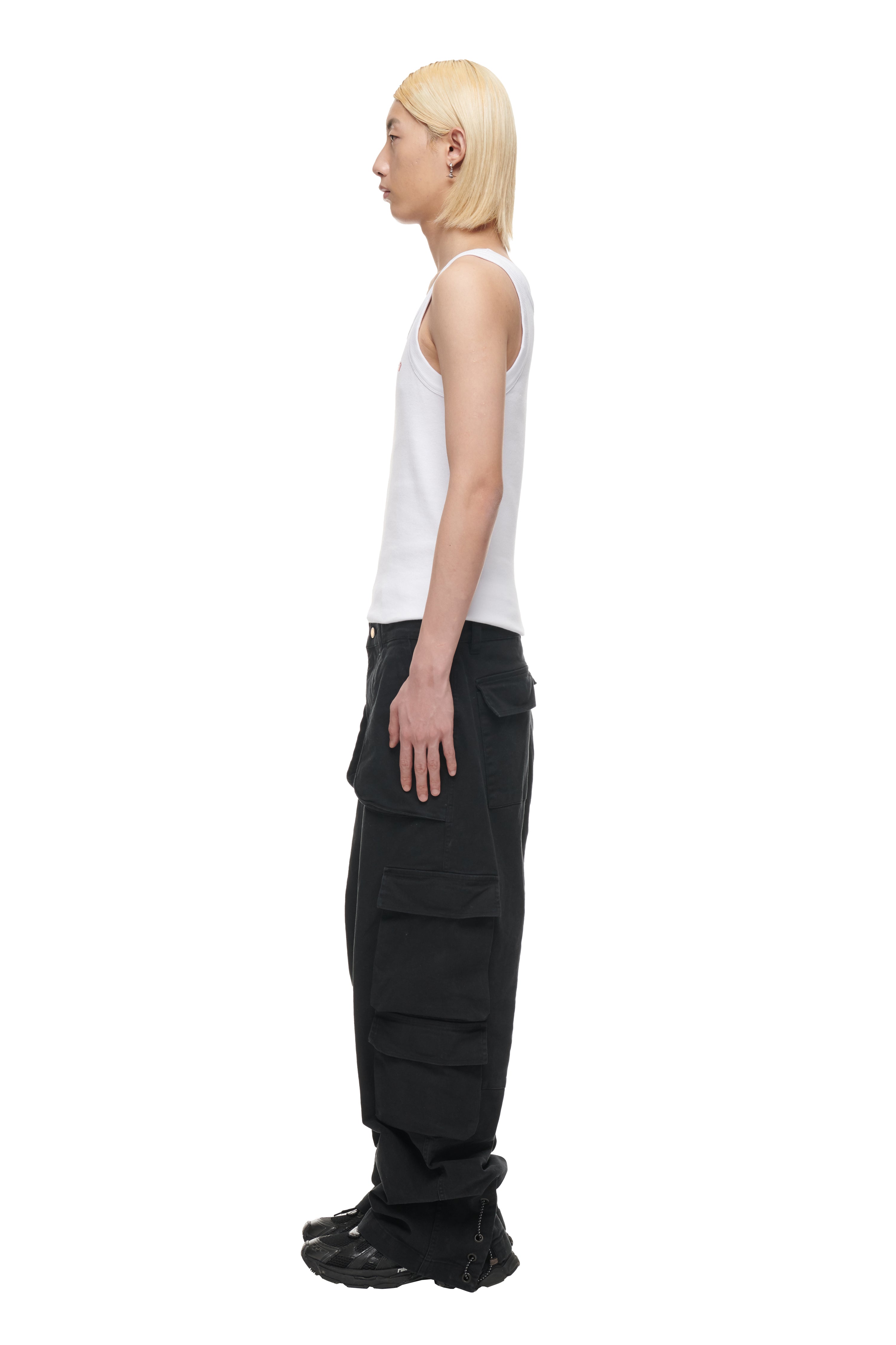 A person with straight, shoulder-length blonde hair stands in profile, wearing a 6PM TANK TOP WHITE (2-PACK), black cargo pants with large pockets, and black sneakers, against a plain white background.