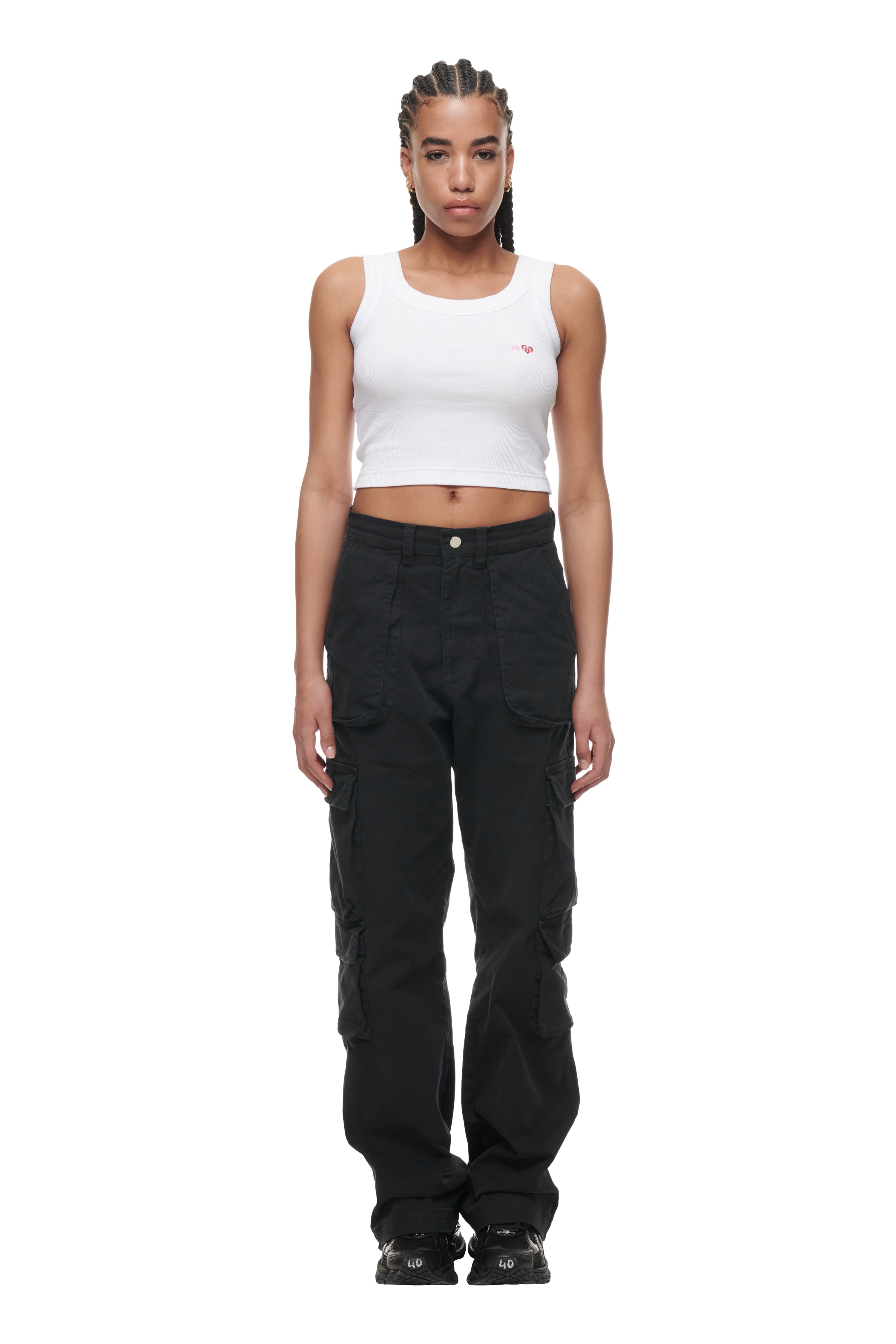 A woman with braided hair wears a 6PM CROP TOP WHITE (2-PACK), black cargo pants, and black sneakers, standing against a plain white background.
