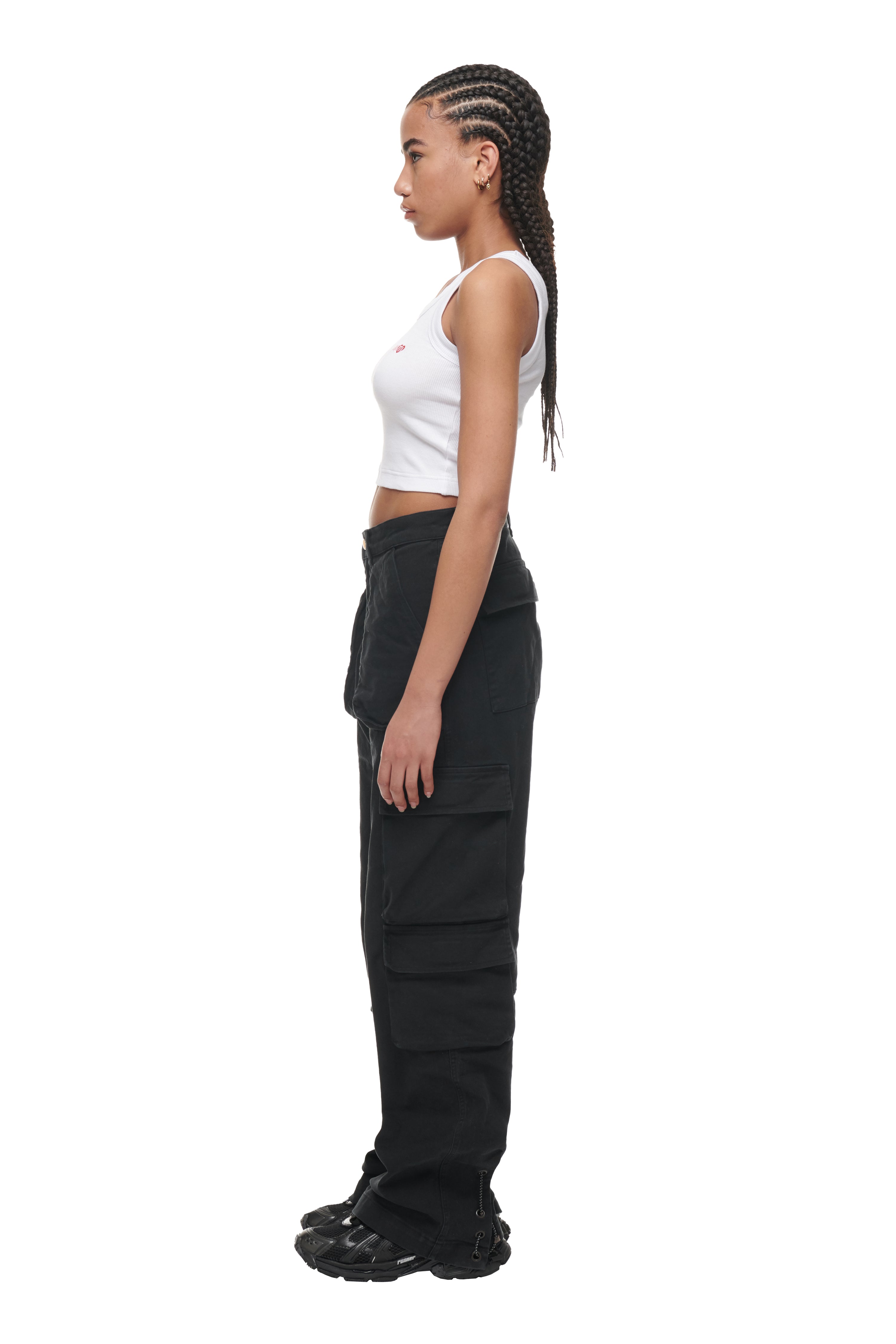 A young woman with braided hair stands in profile wearing a 6PM CROP TOP WHITE (2-PACK), black cargo pants with large pockets, and black sandals, against a plain white background.