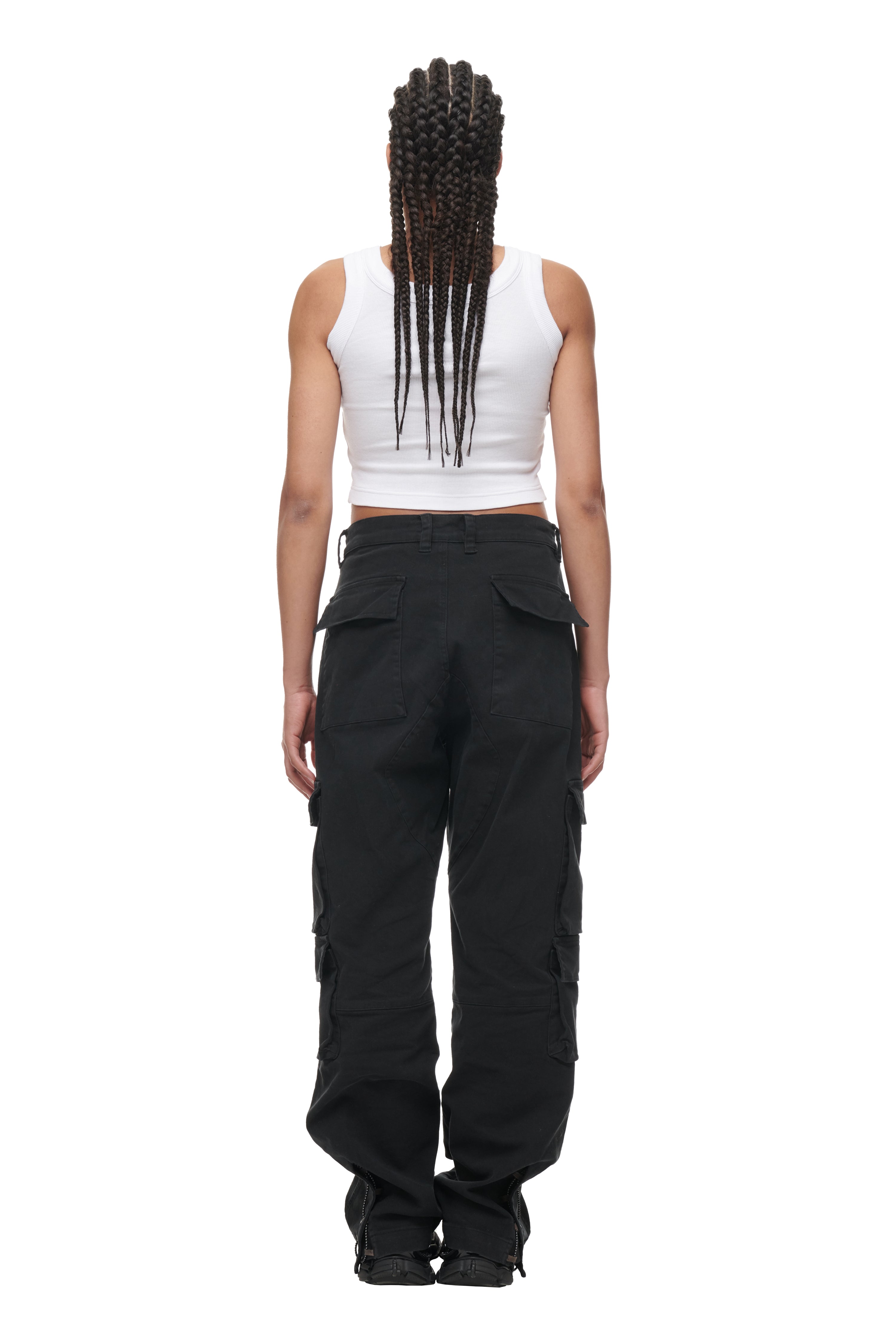 A person with long, braided hair stands with their back to the camera, wearing the 6PM CROP TOP WHITE (2-PACK) and loose black cargo pants, against a white background.