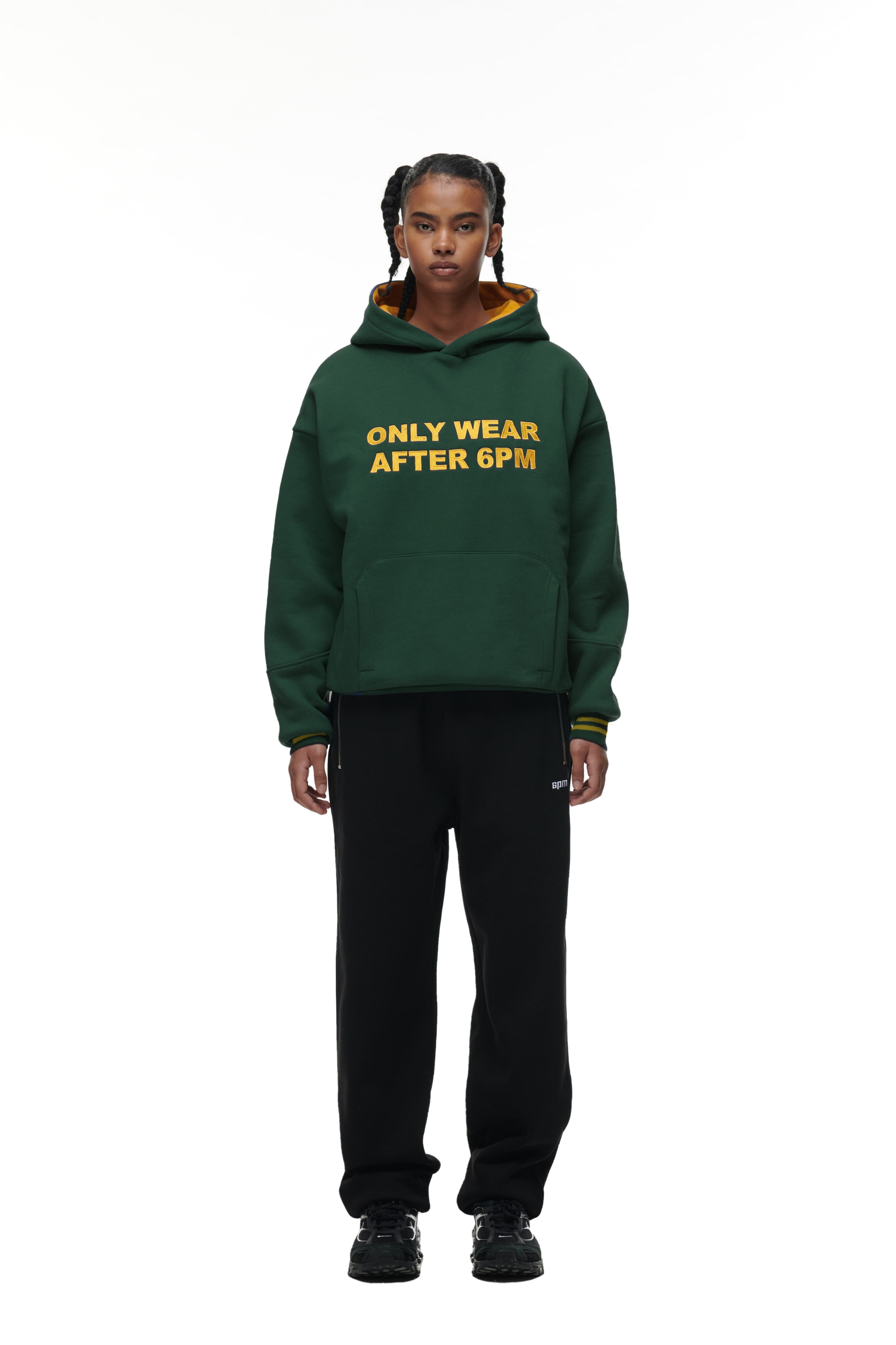 A person stands facing forward wearing the 6PM ONLY WEAR HOODIE GREEN with yellow text, paired with black pants and black sneakers, against a plain white background.
