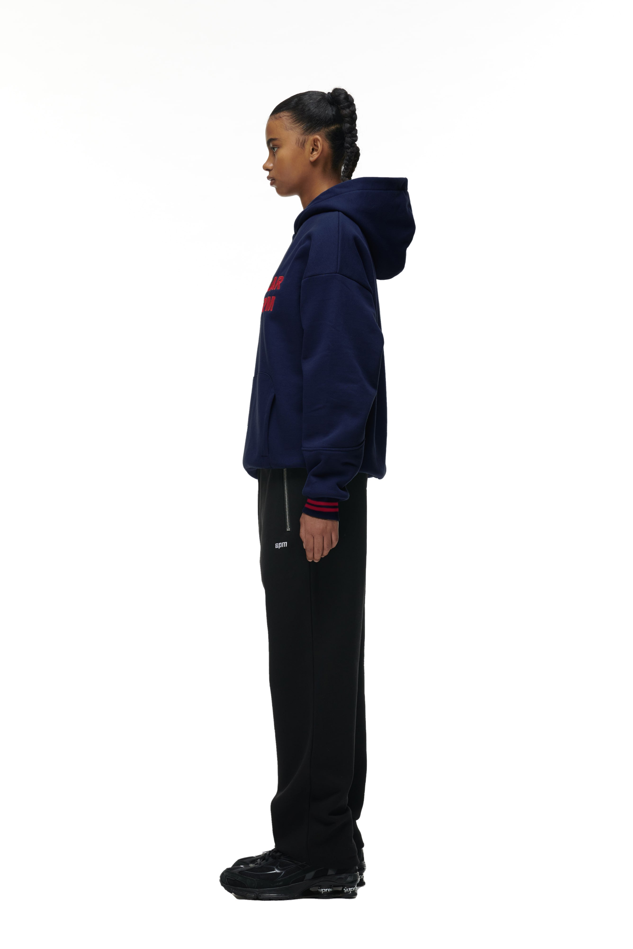 A person stands in profile against a white background, wearing the 6PM ONLY WEAR HOODIE NAVY, black pants, and black sneakers. Their hair is pulled back, and their hands rest by their sides.