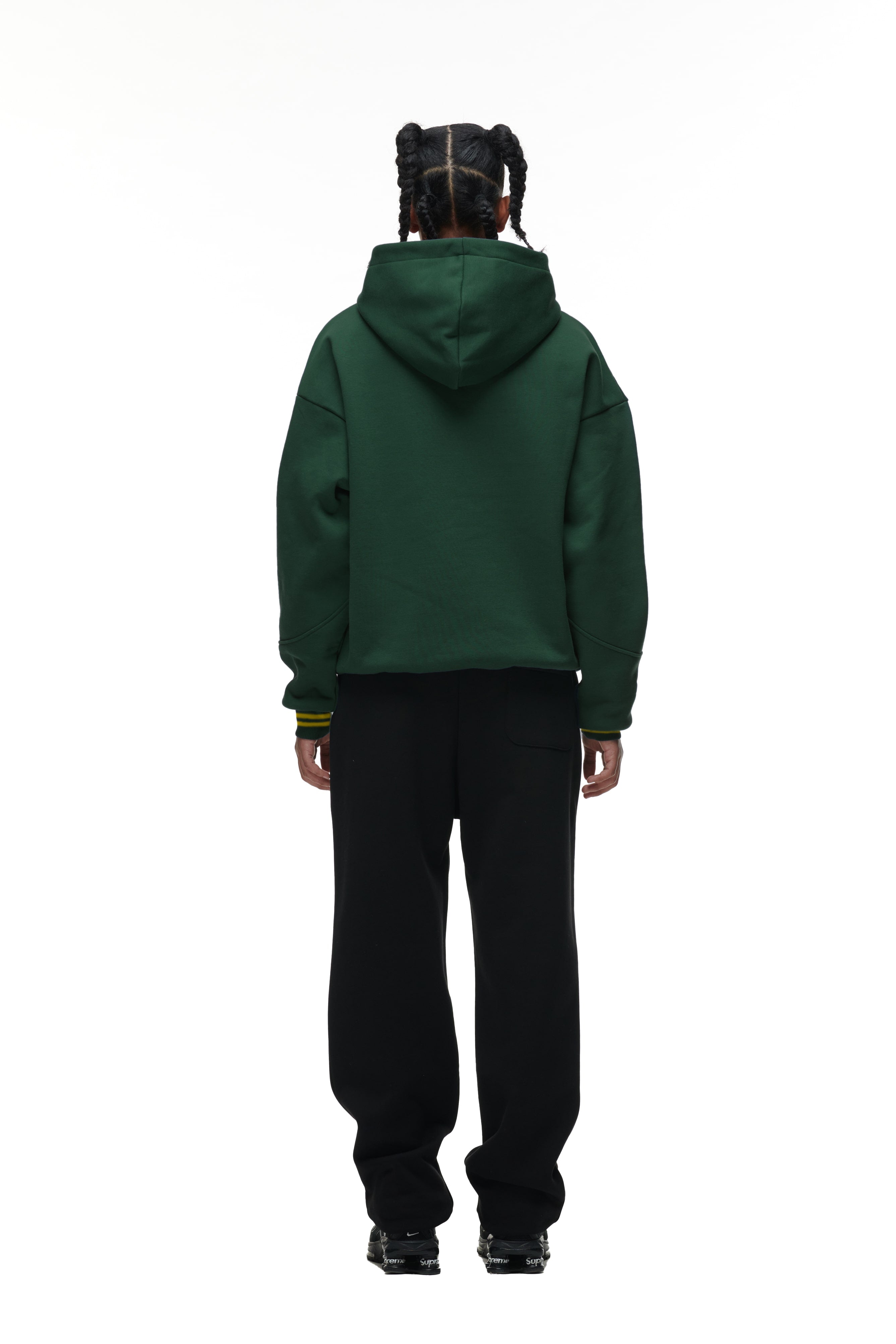 A person with braided hair, seen from behind, wears the 6PM ONLY WEAR HOODIE GREEN and black pants against a plain white background.