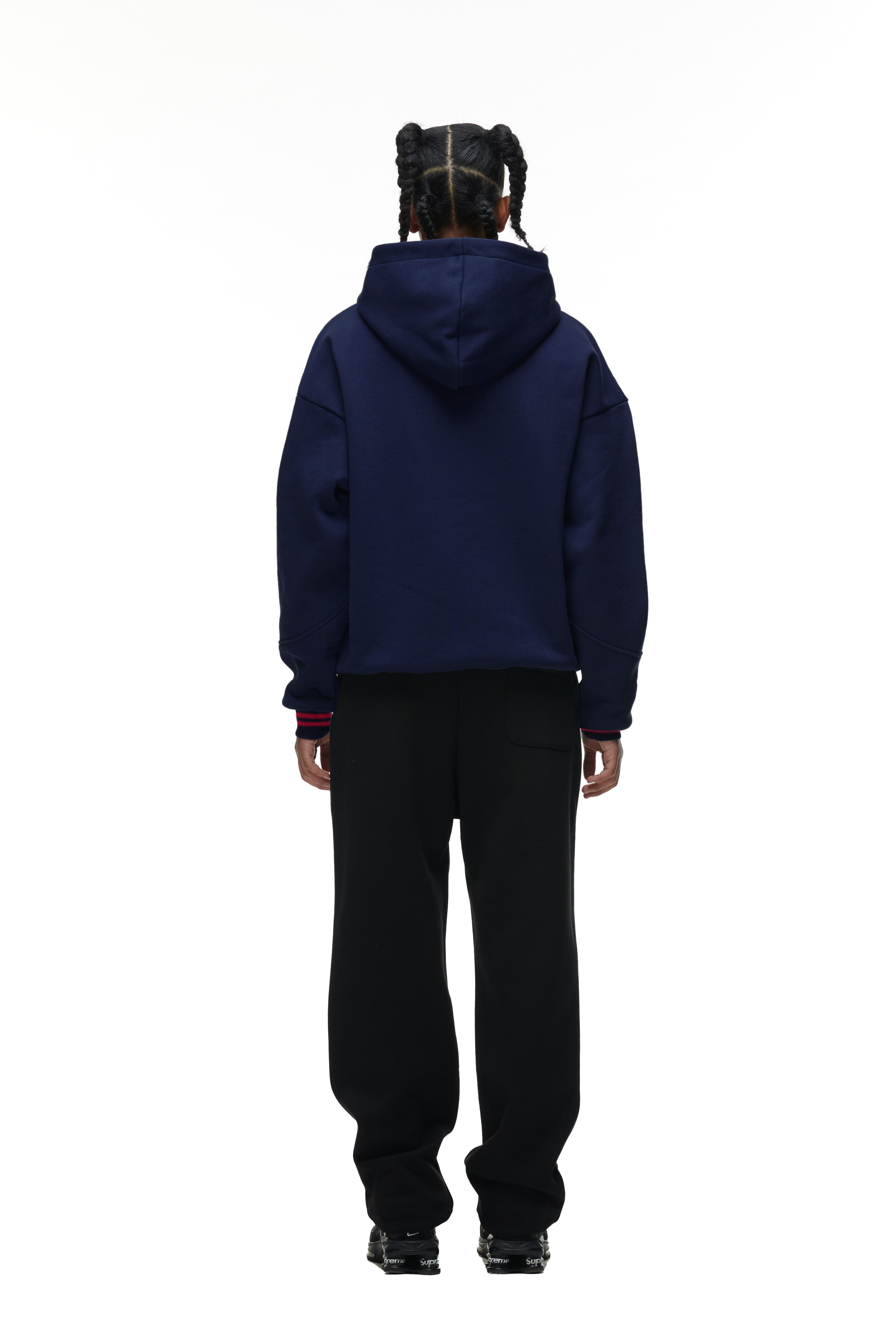 A person with braided hair, facing away, wears the 6PM ONLY WEAR HOODIE NAVY with black pants and black sneakers against a plain white background.