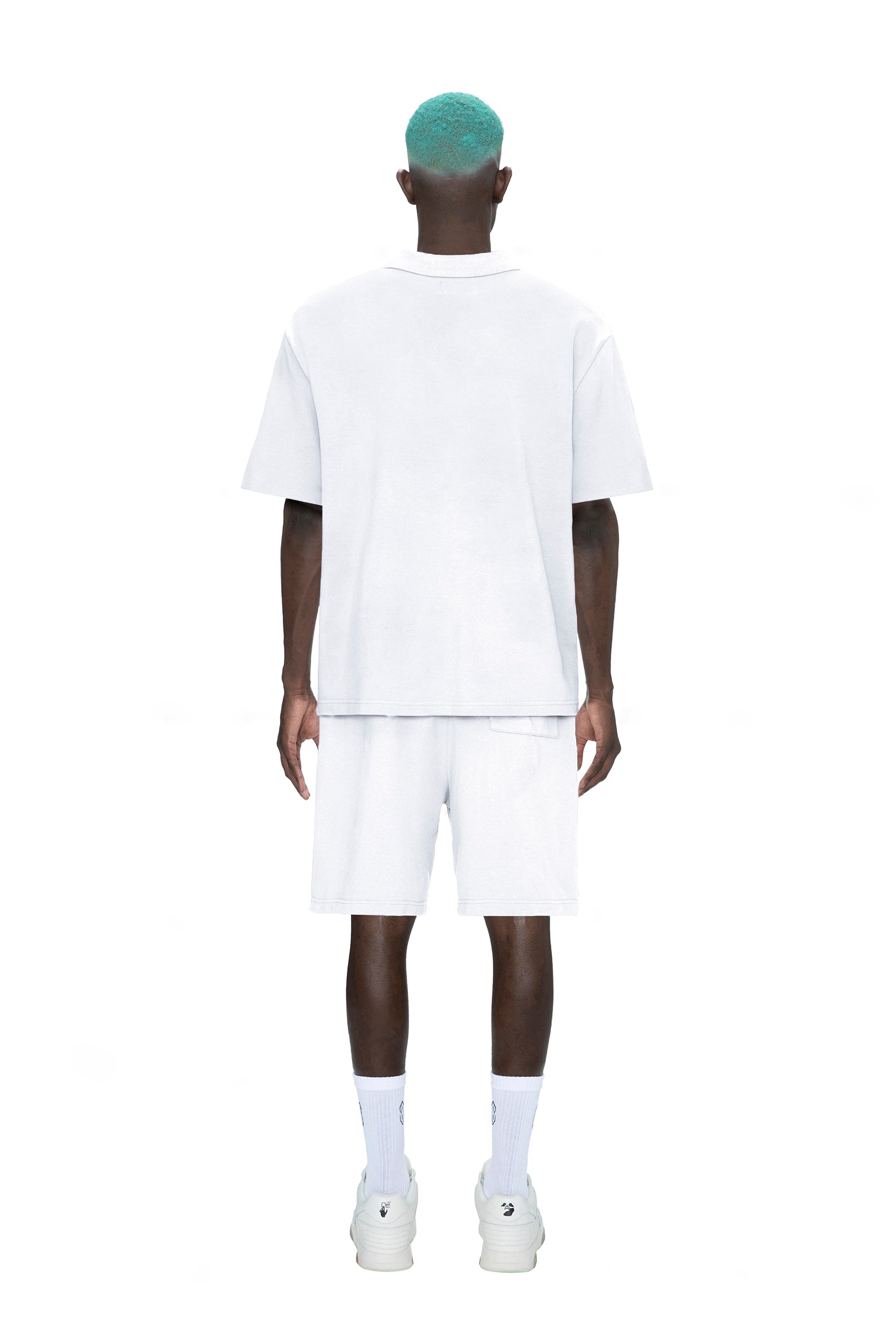 A person with teal hair stands facing away, wearing a 6PM POLO SHIRT WHITE, white shorts, socks, and sneakers against a plain white background.