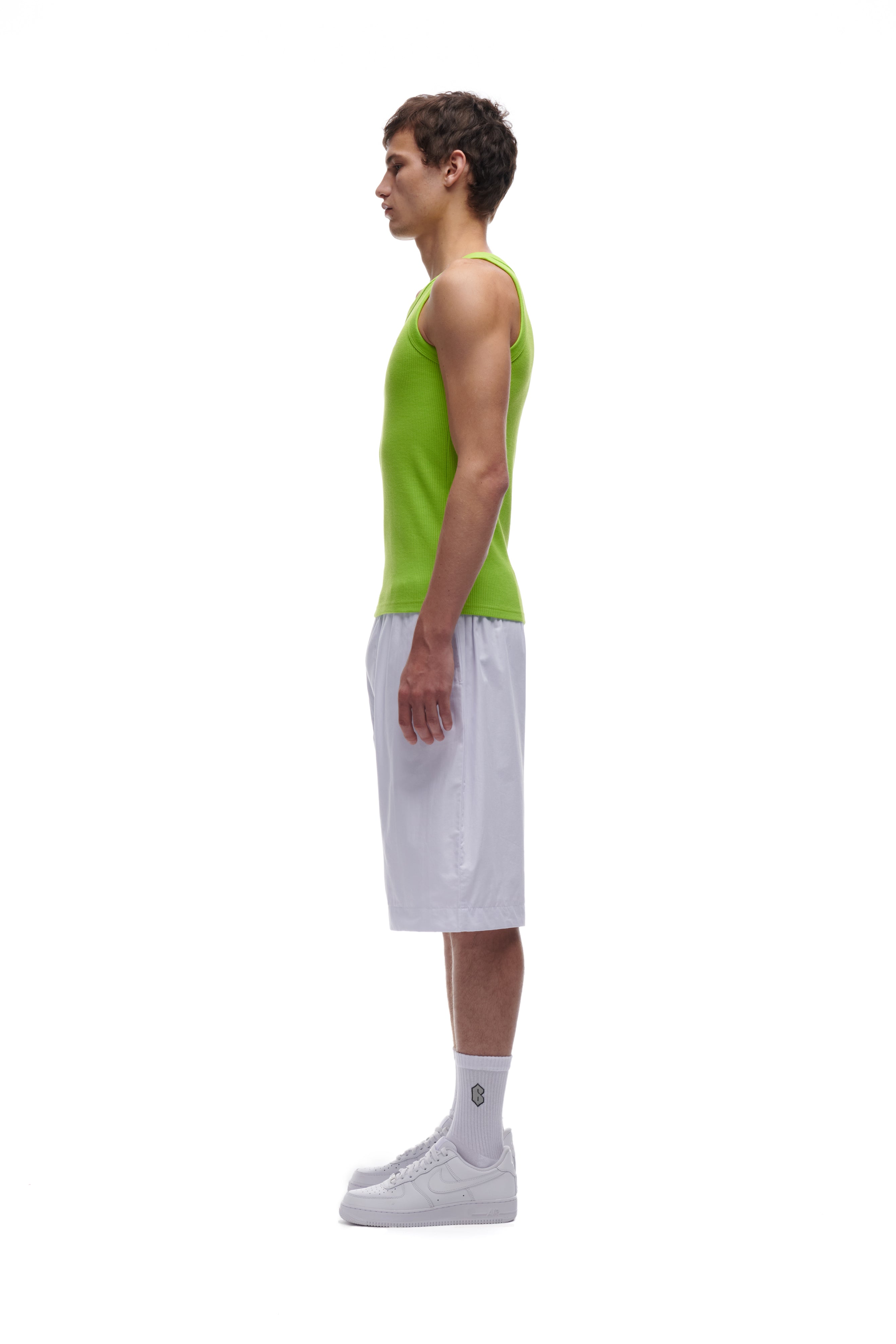 A young man stands in profile against a white background, wearing the 6PM WAFFLE KNIT TANK TOP LIME GREEN, paired with white basketball shorts, crew socks, and sneakers.