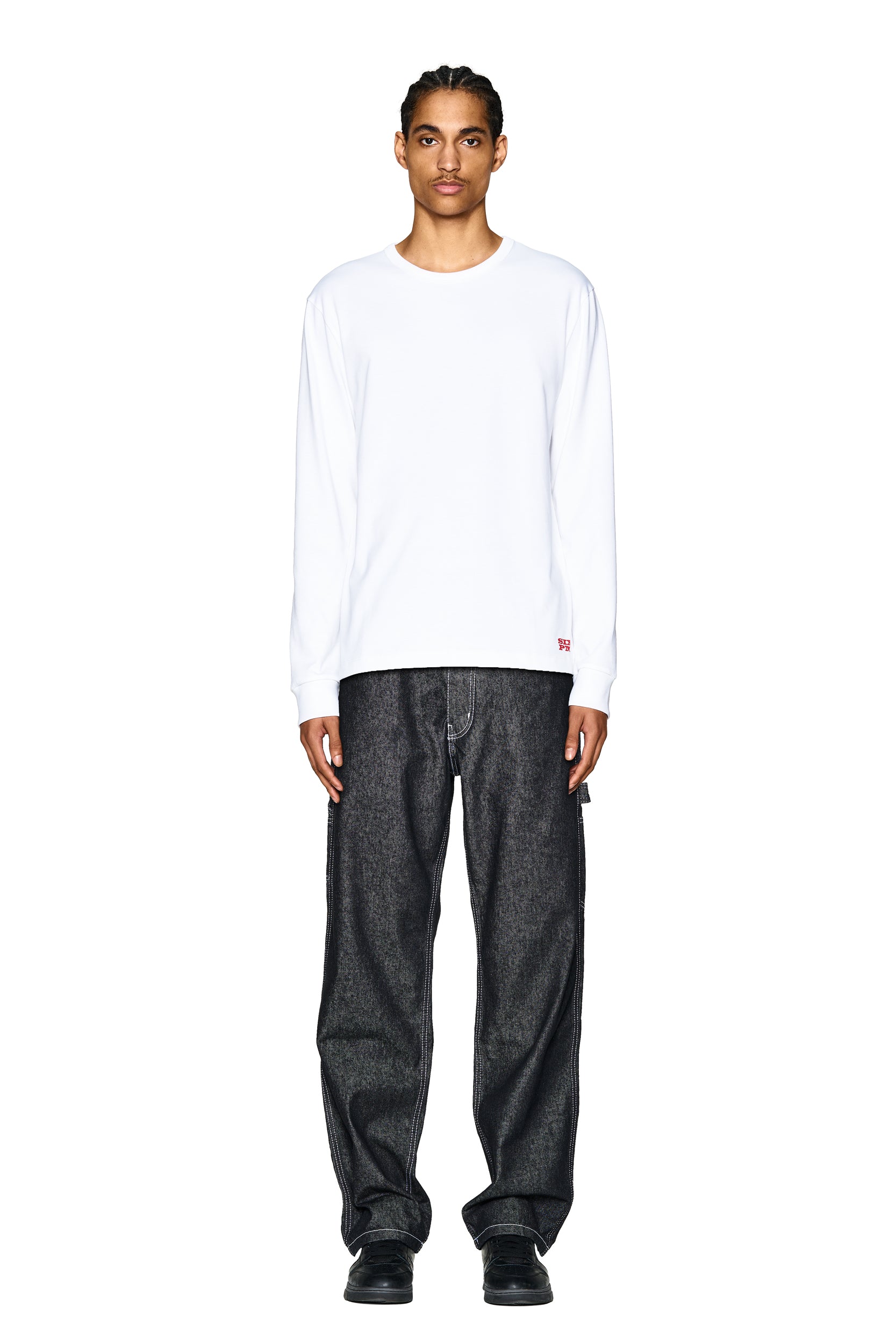 A person stands facing forward against a white background, wearing the 6PM DEVIL LONG SLEEVE WHITE shirt, loose-fitting dark jeans, and black shoes.