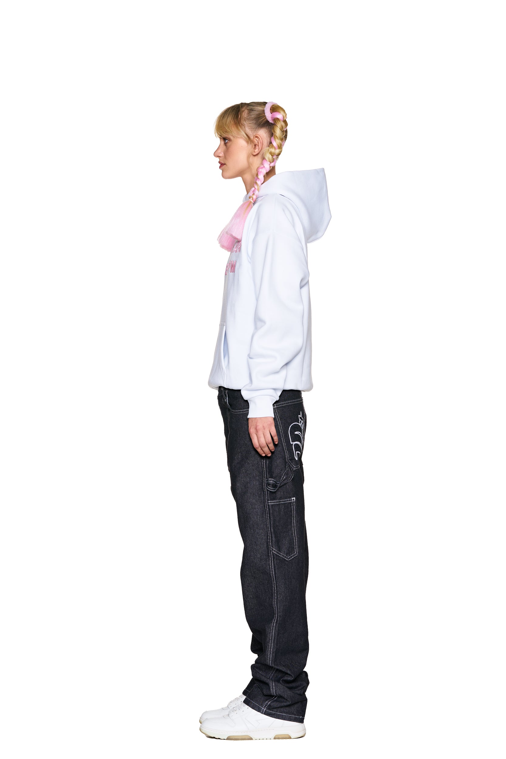 A person with blond braided hair stands in profile against a white background, wearing the 6PM ONLY WEAR AFTER 6PM HOODIE 2.0 WHITE, black jeans with a white pocket design, and white sneakers.